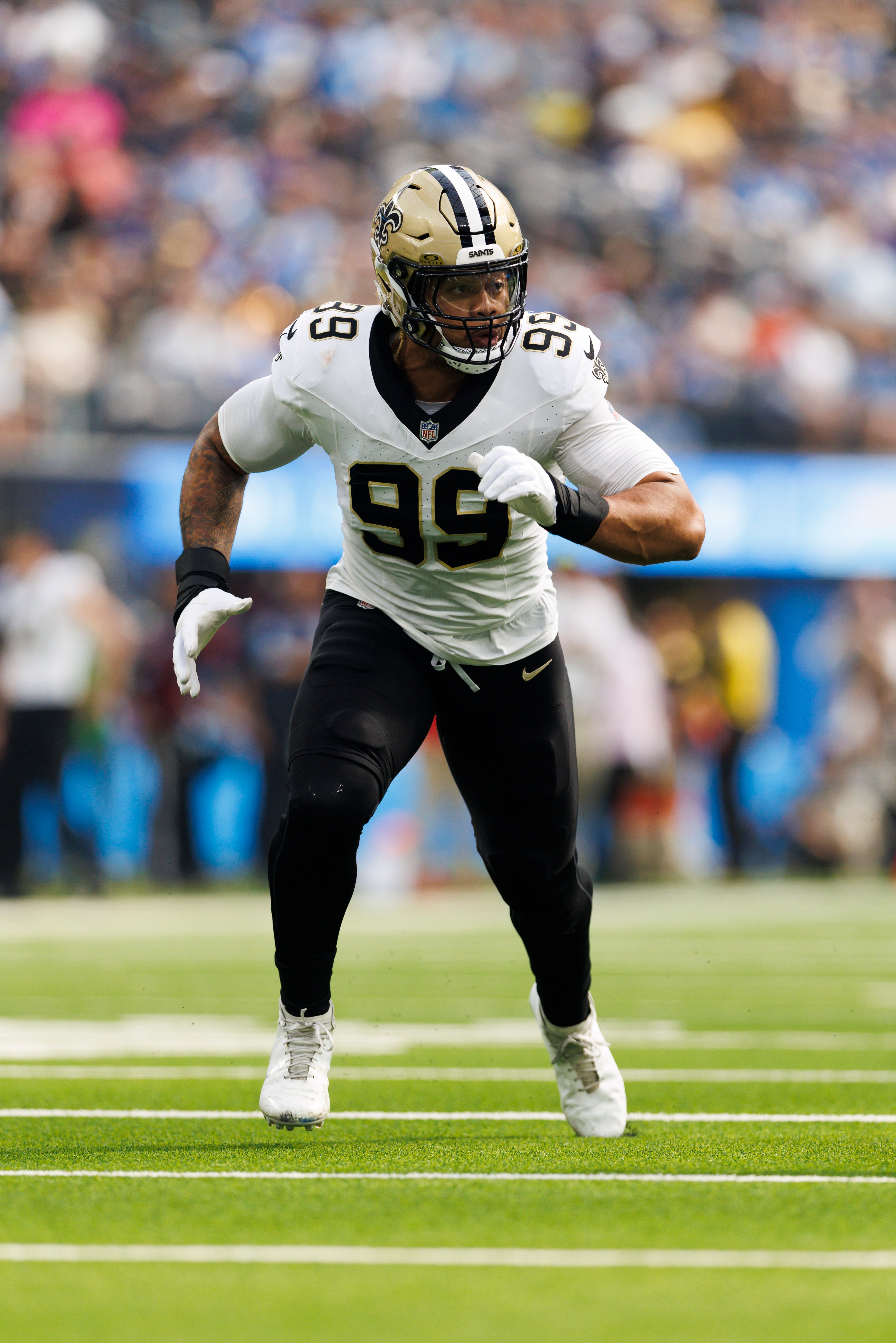 A football player in a white and black uniform with the number 99 runs on a green field. He wears a helmet and white cleats, with a blurred crowd in the background.