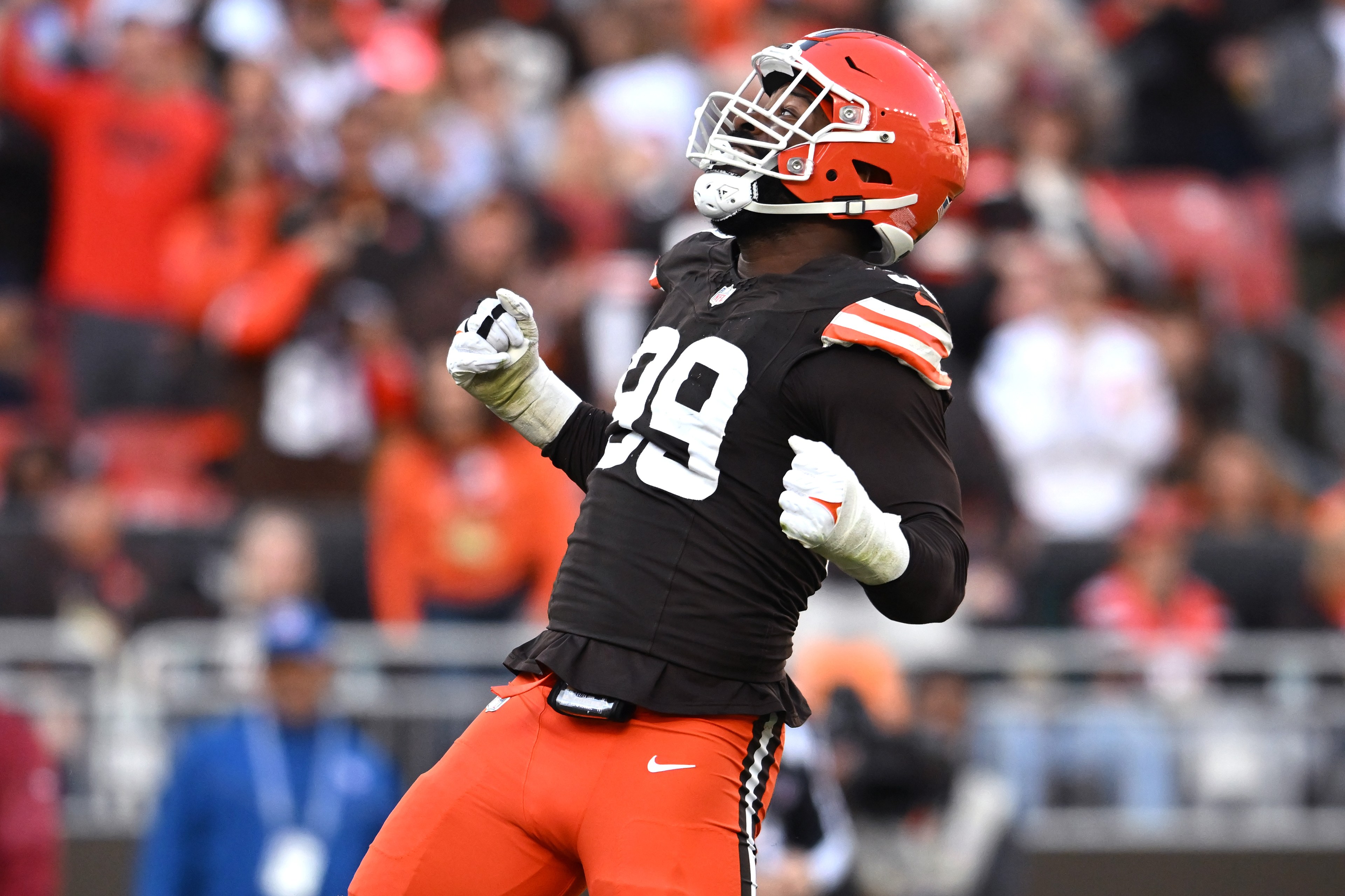 A football player wearing a black jersey with number 99 and orange pants celebrates energetically on the field, with an orange helmet and clenched fists.