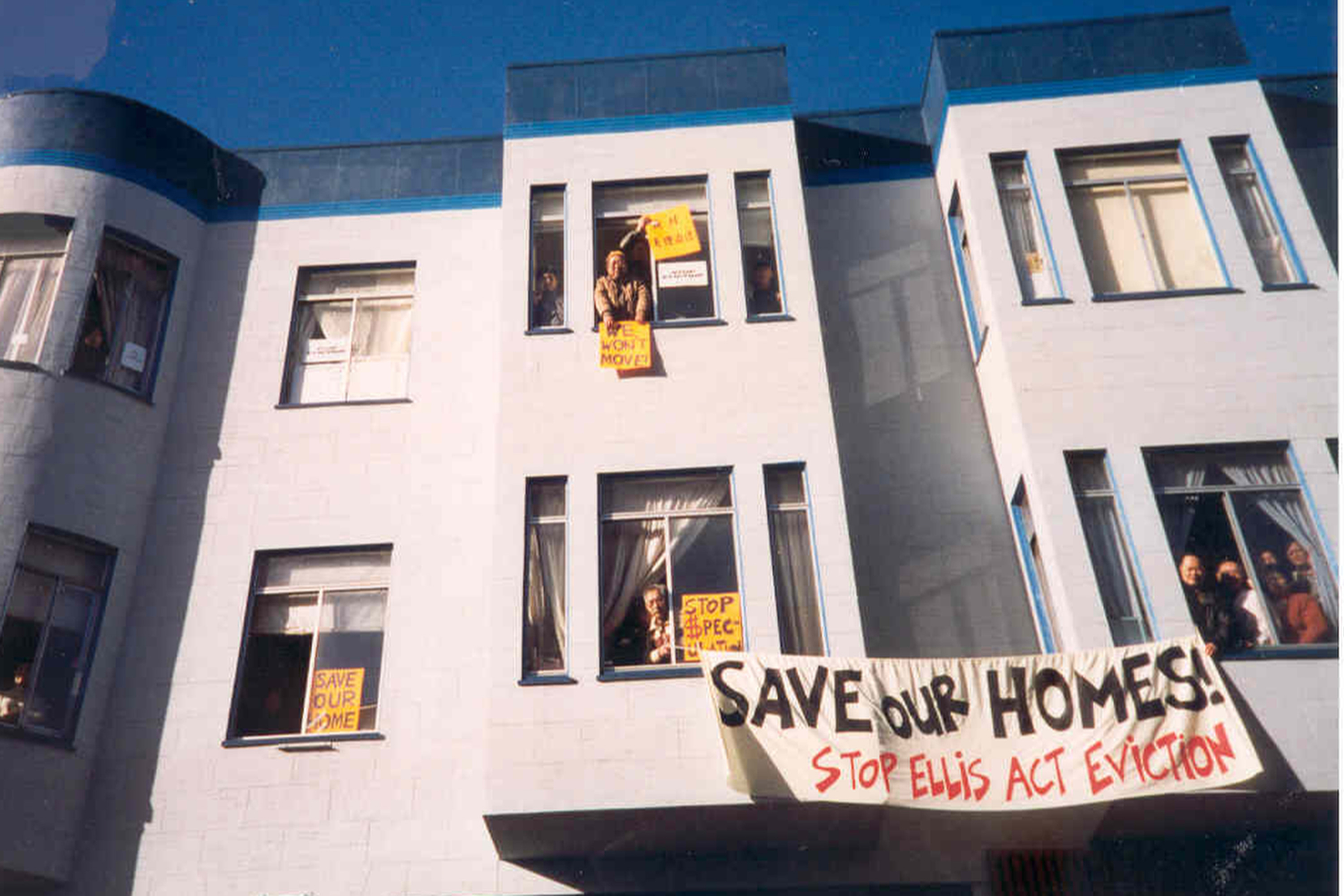 A photo of an apartment building with protest signs hanging out of it reading &quot;save our homes!&quot; 