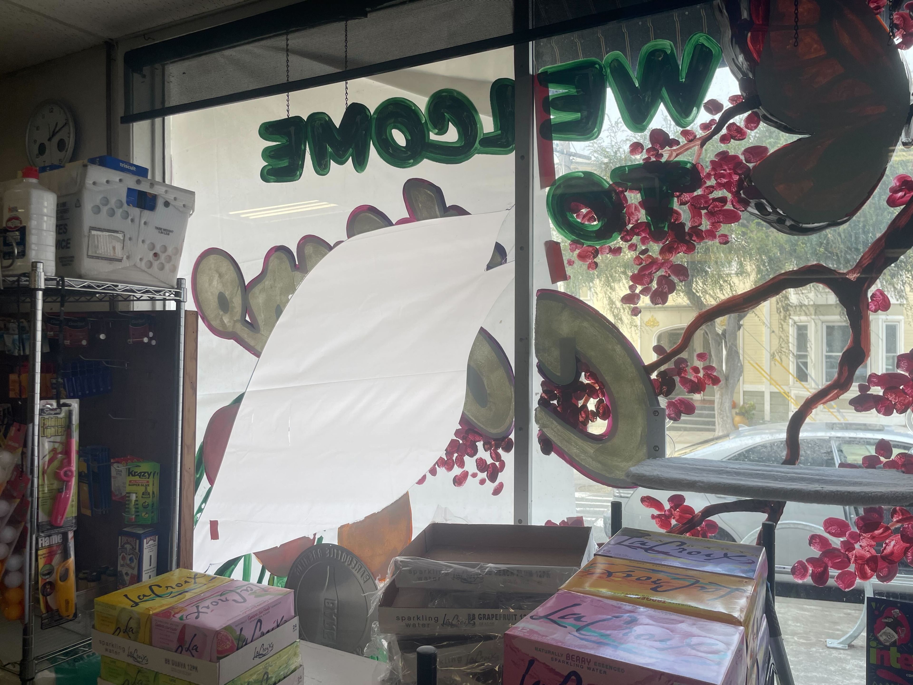 A store window displays decorative lettering with pink flowers, and boxes of LaCroix are stacked inside. Shelves with various products are visible beside the window.