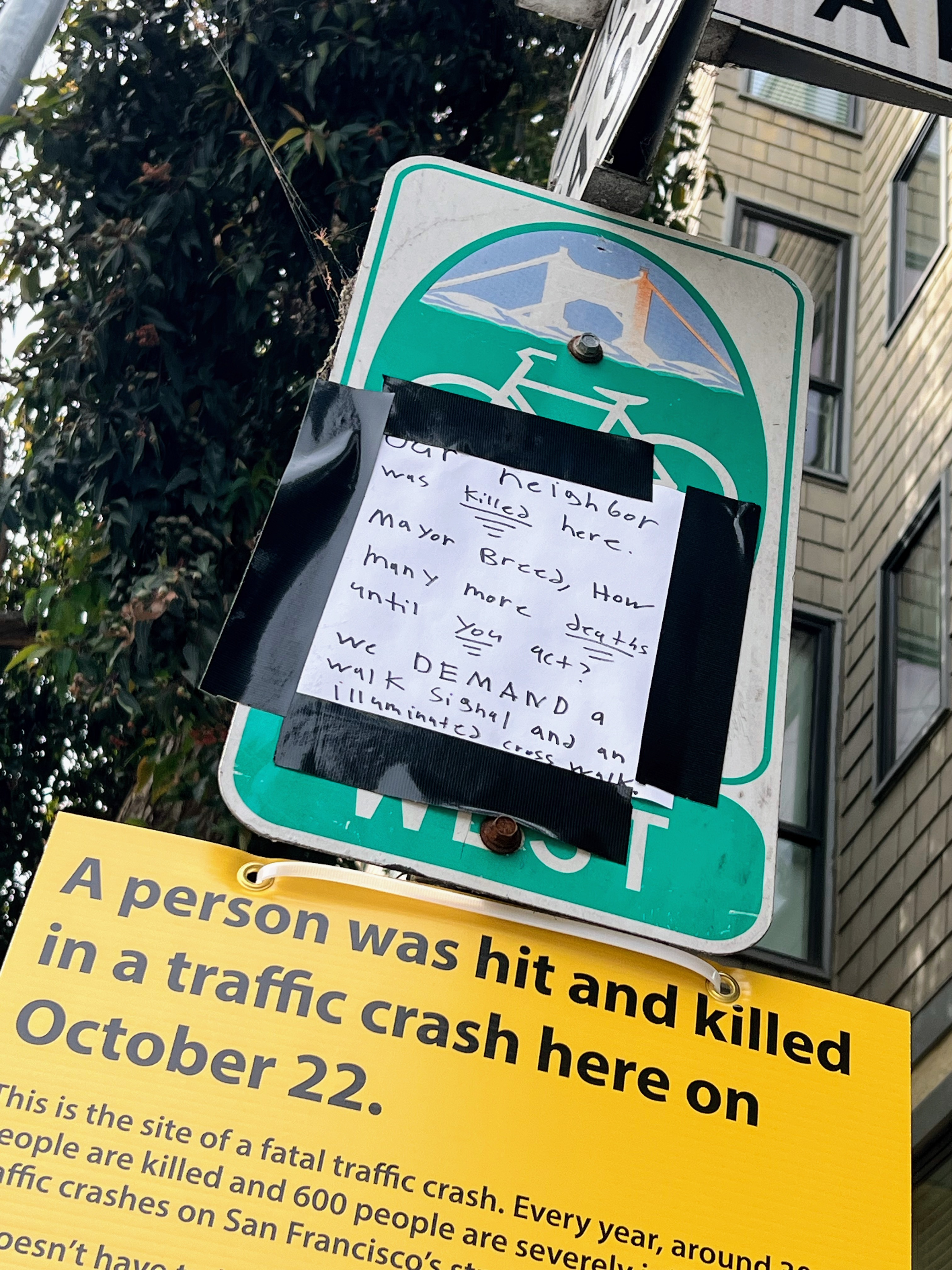 A bicycle sign has handwritten and printed notices attached, detailing a fatal traffic accident and demanding safety improvements.