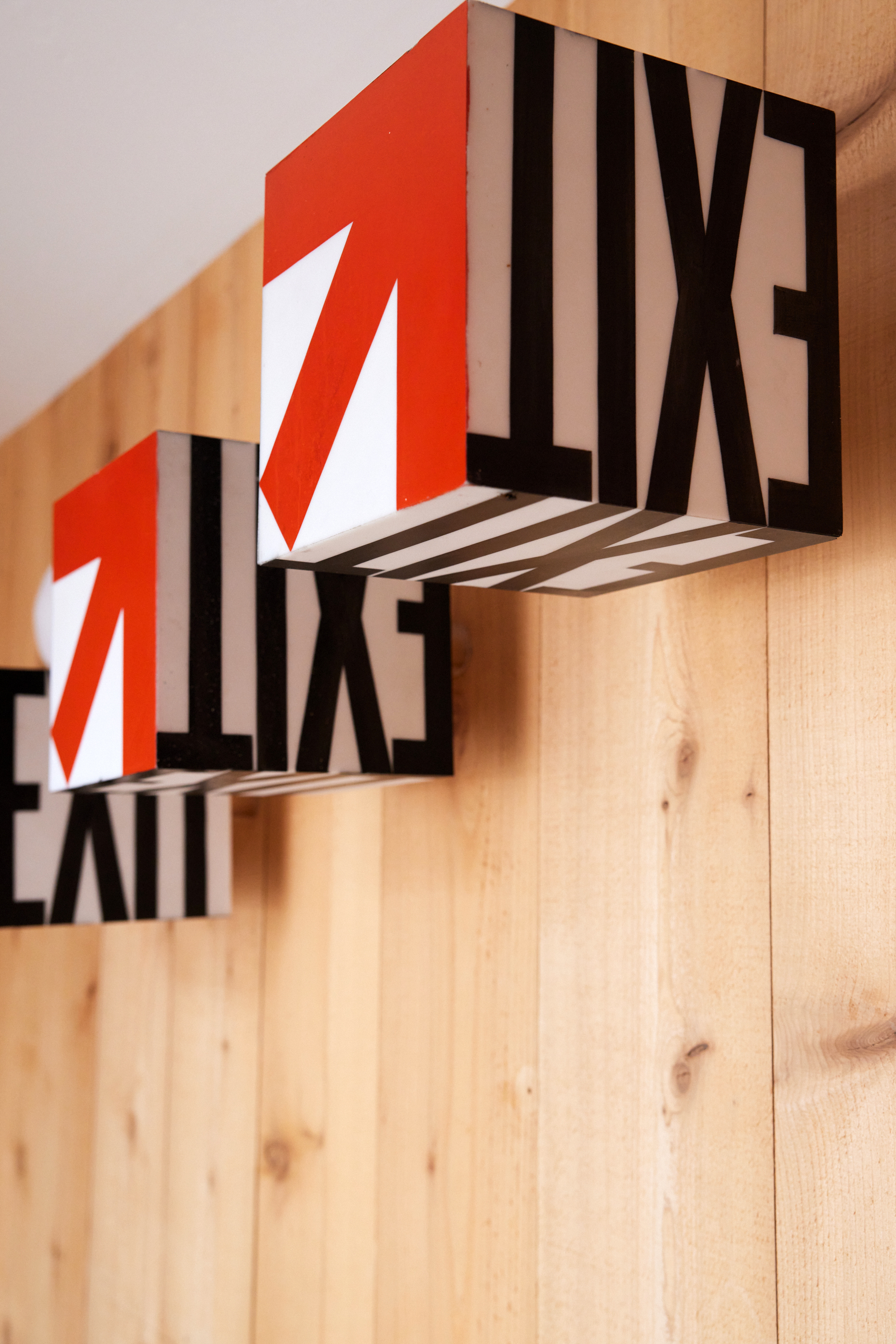 The image shows three cube-shaped &quot;EXIT&quot; signs with red arrows, mounted sideways on a wooden wall.