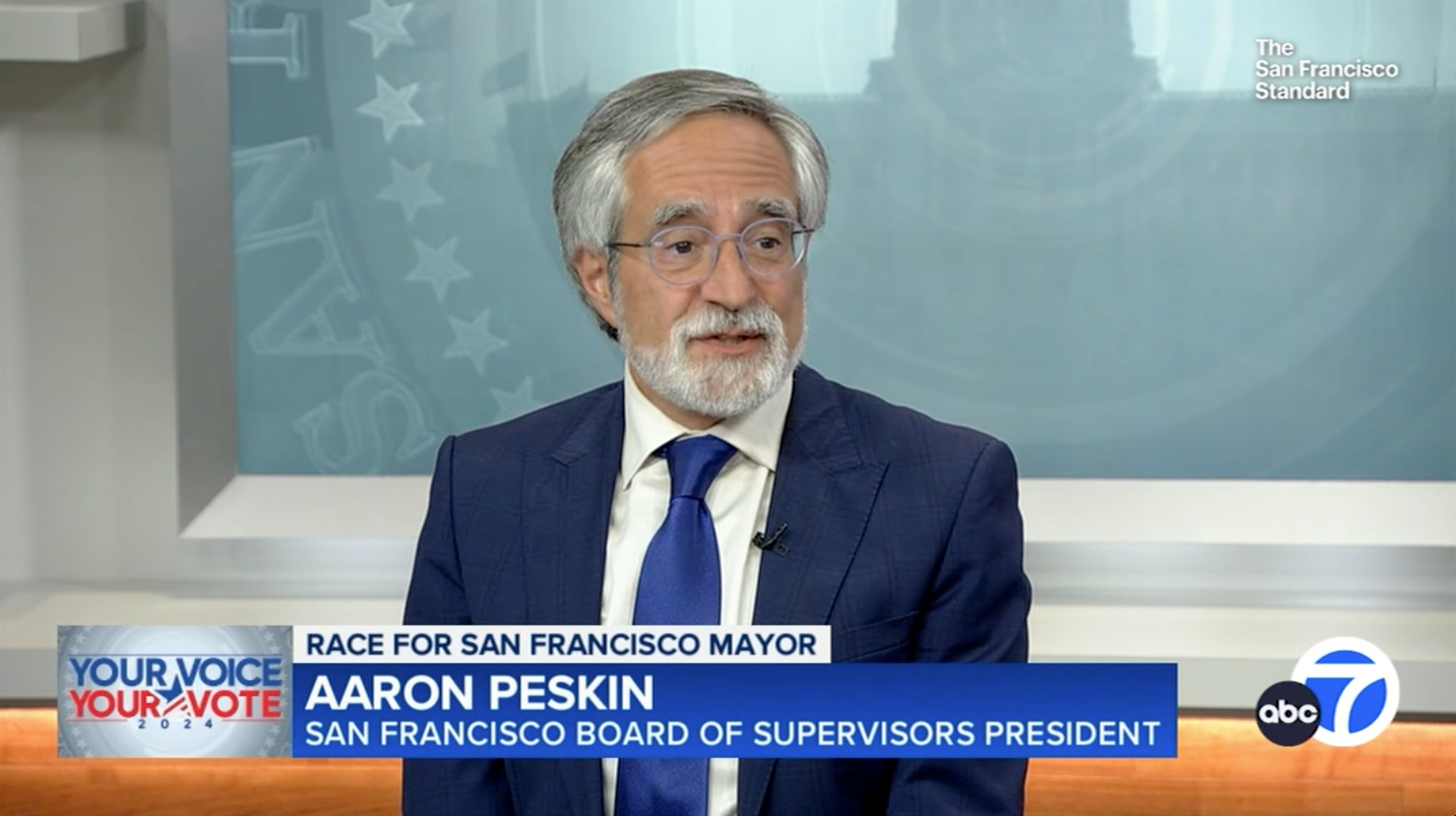 A man with gray hair and glasses in a blue suit and tie is speaking on a news show about the San Francisco mayoral race. The text identifies him as Aaron Peskin.