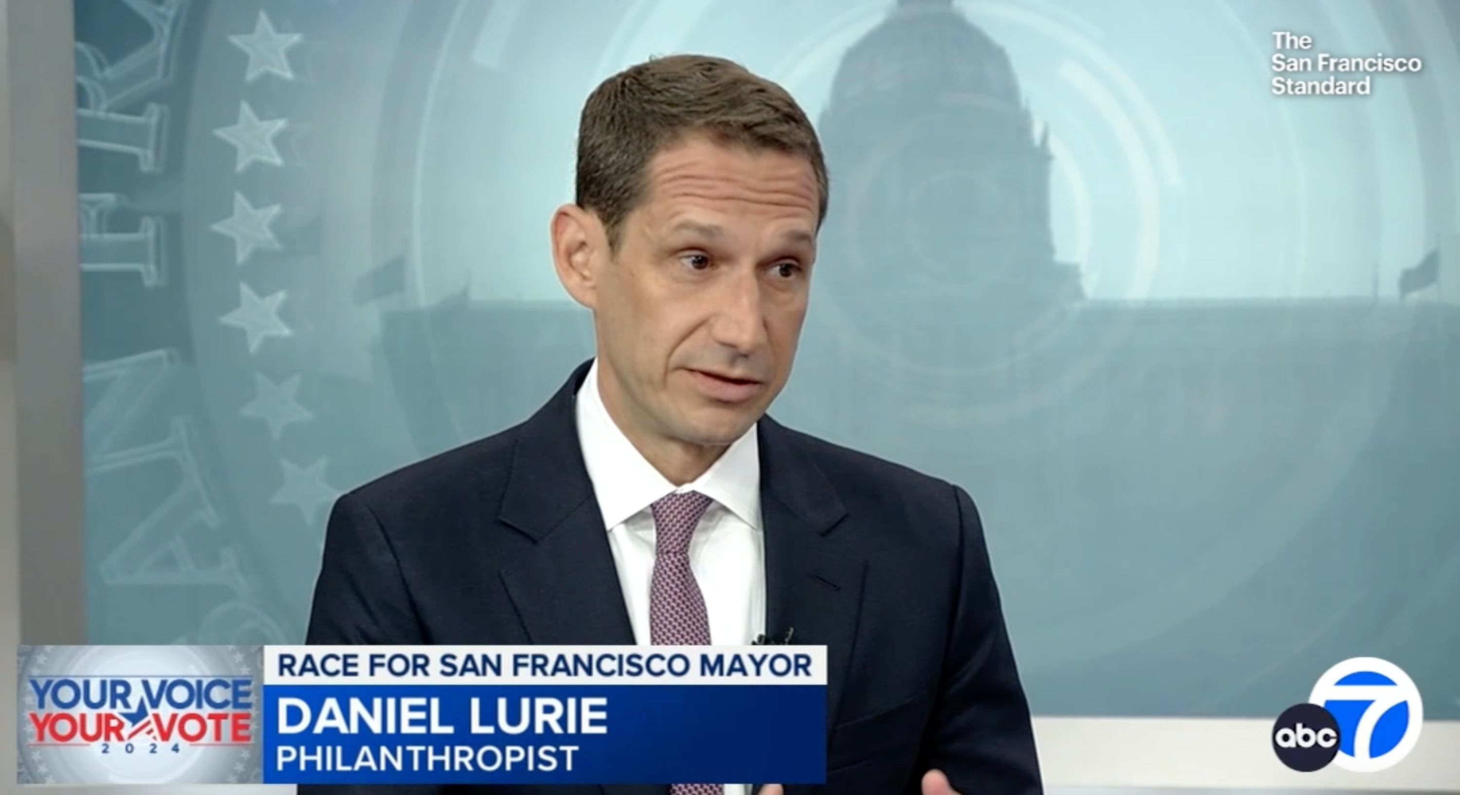 A man in a suit is shown in a TV news interview; the caption reads &quot;Daniel Lurie, Philanthropist,&quot; discussing the &quot;Race for San Francisco Mayor.&quot;