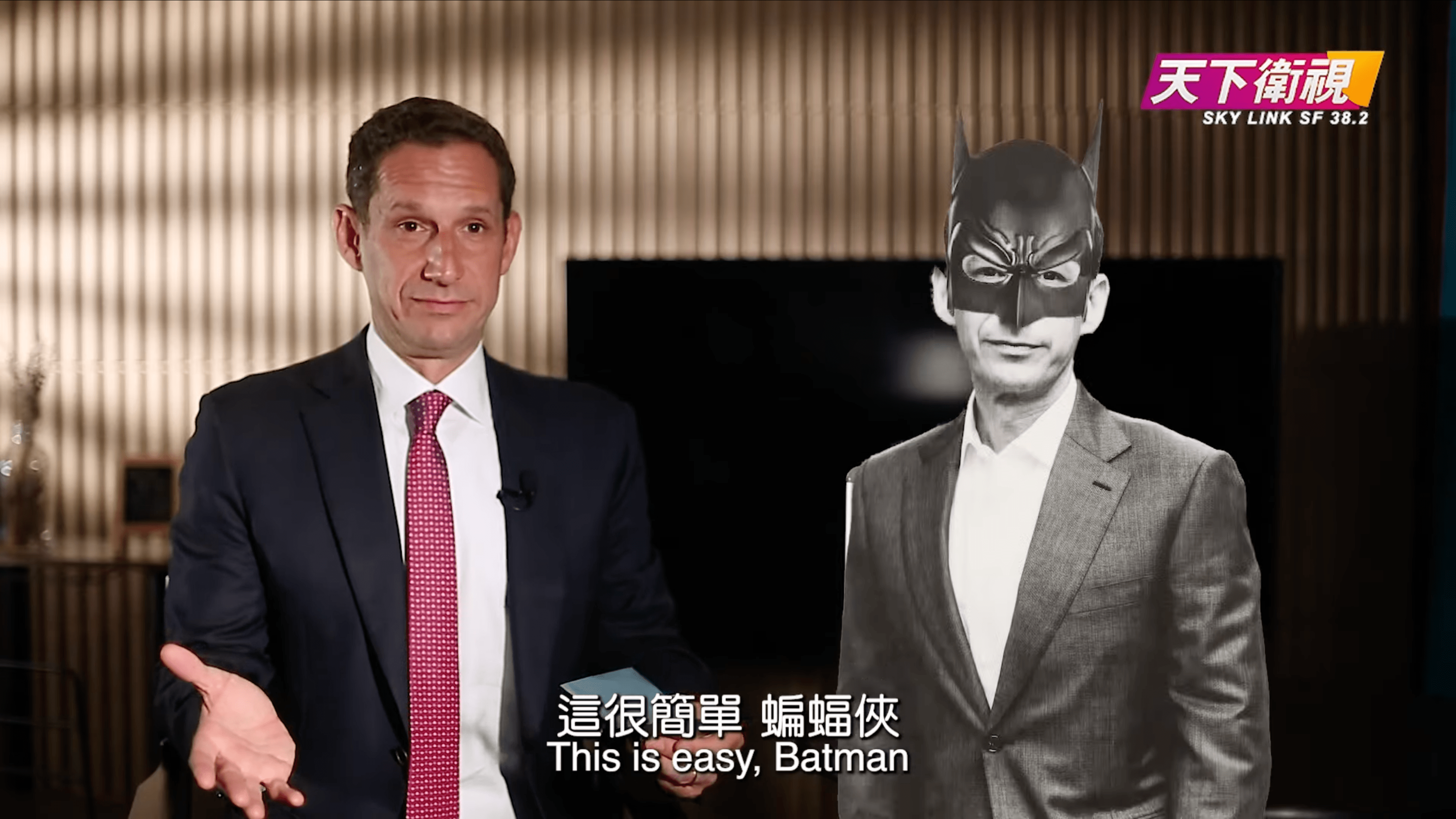 A man in a suit gestures with his hand, while a black-and-white photo of another man wearing a Batman mask stands near him. Subtitles read &quot;This is easy, Batman.&quot;