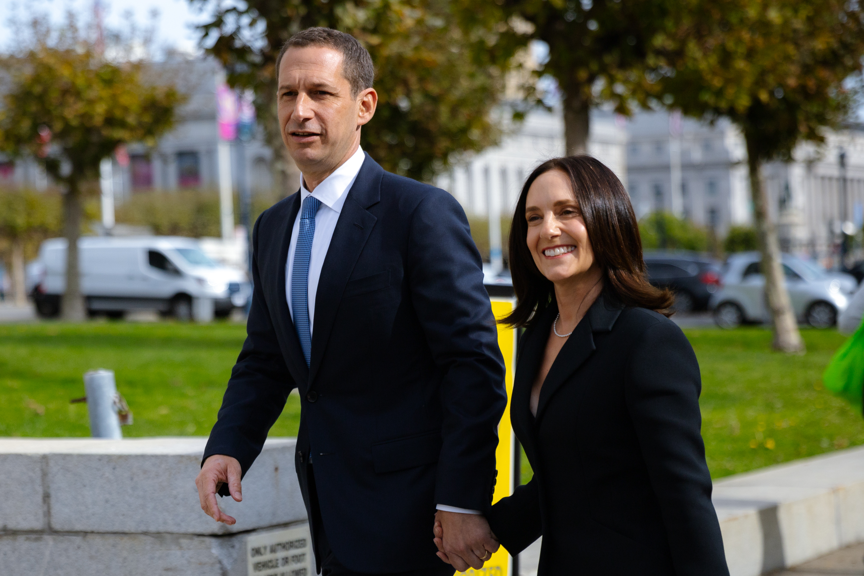 A man and woman in a suit hold hands while walking into a building. 