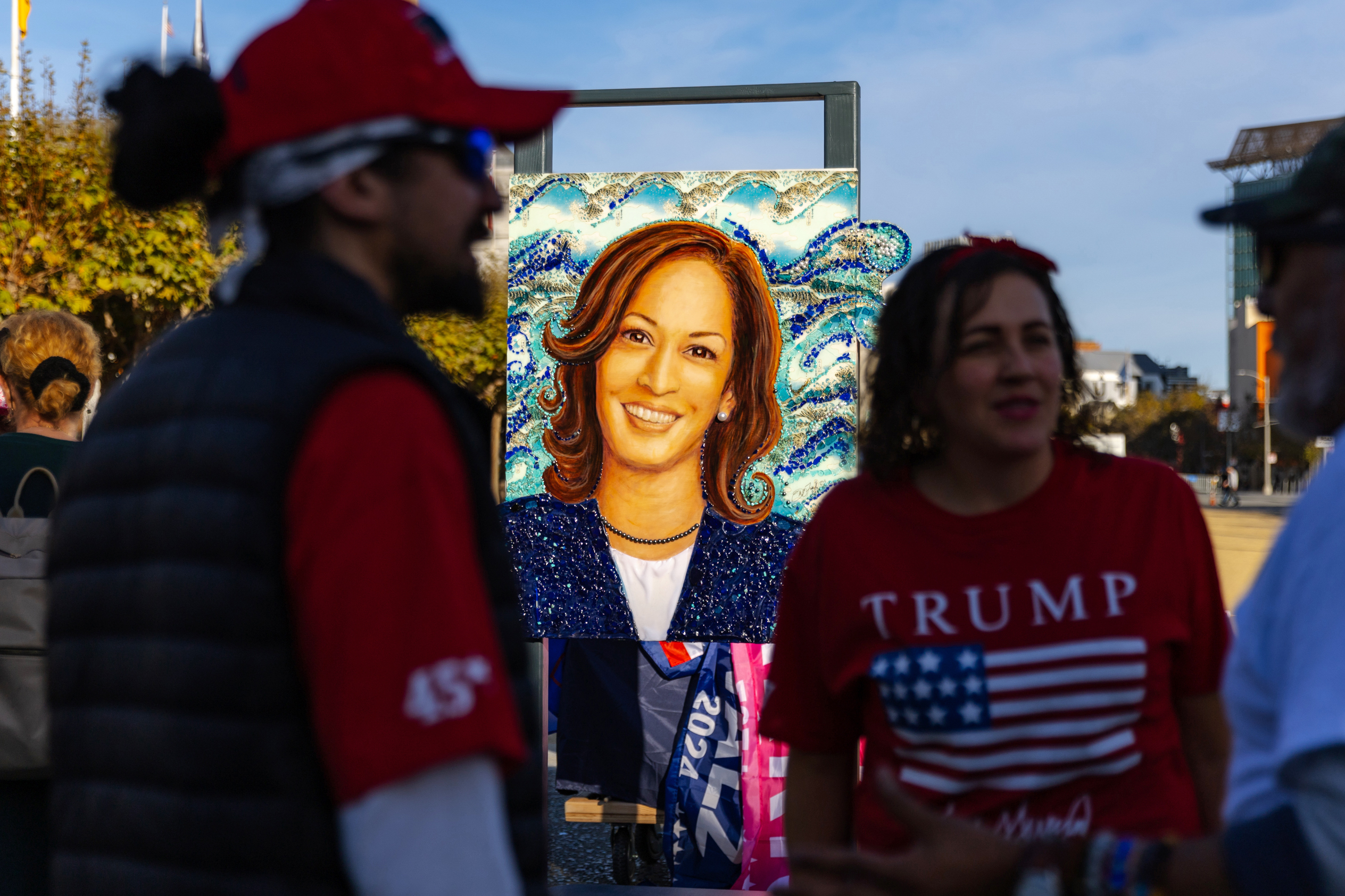 The image shows a vibrant portrait of a woman with curly hair, smiling brightly against a swirling blue background, surrounded by people in Trump-themed attire.