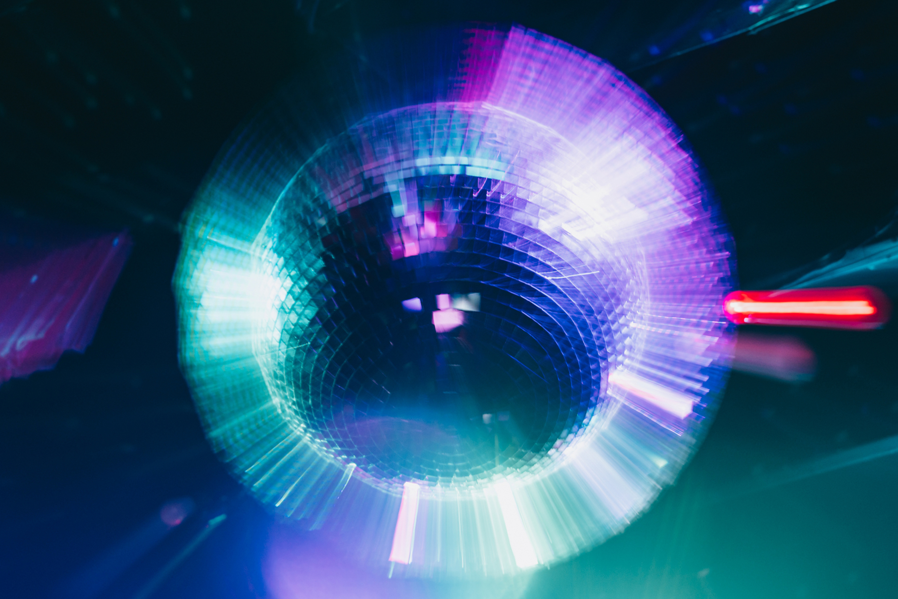 A spinning disco ball reflects vibrant colors, mostly blues and purples, creating a dynamic and lively light display in a darkened room.