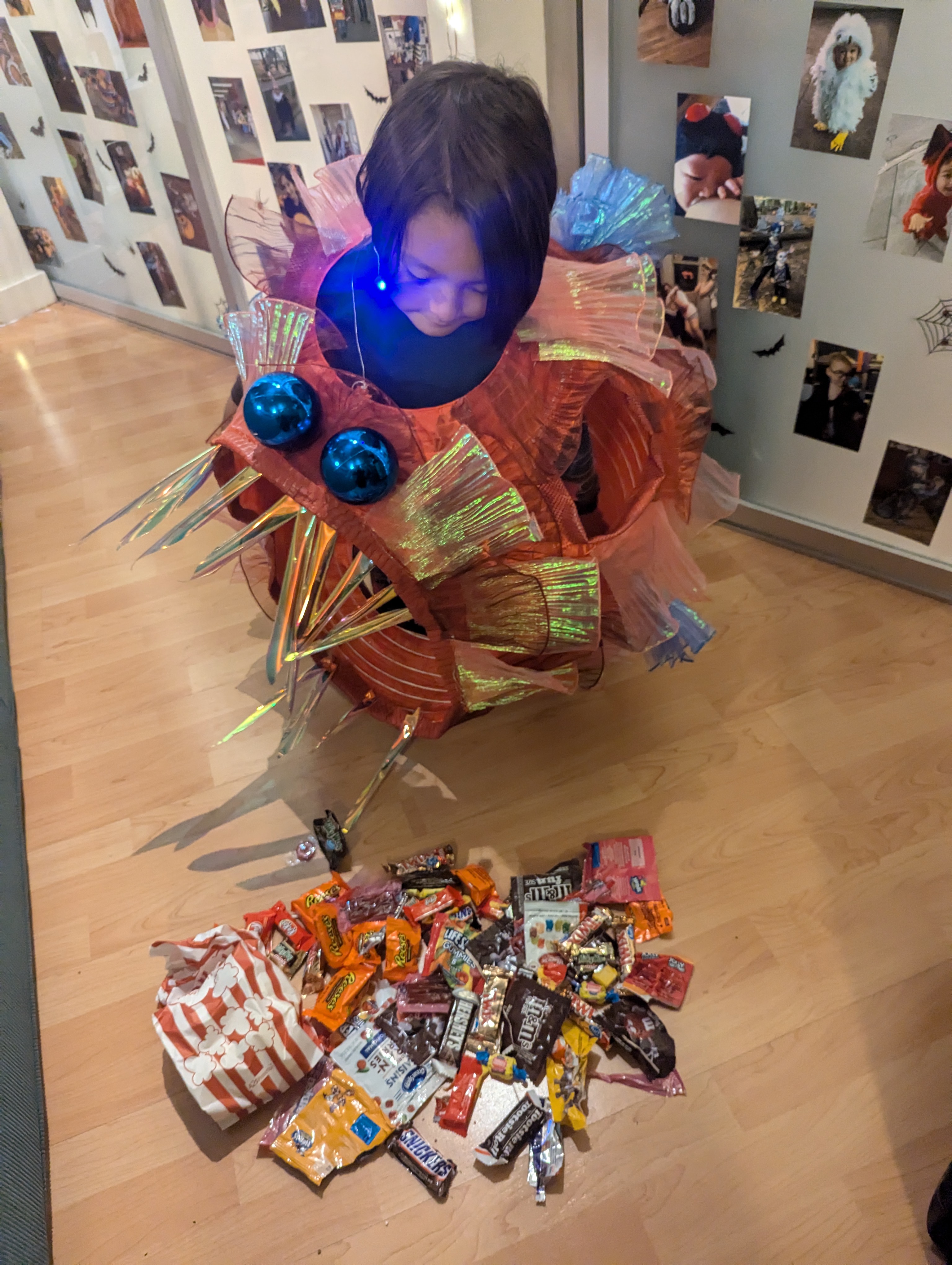 A kid in a homemade orange Anglerfish costume looks down at a spread of multicolored candy.