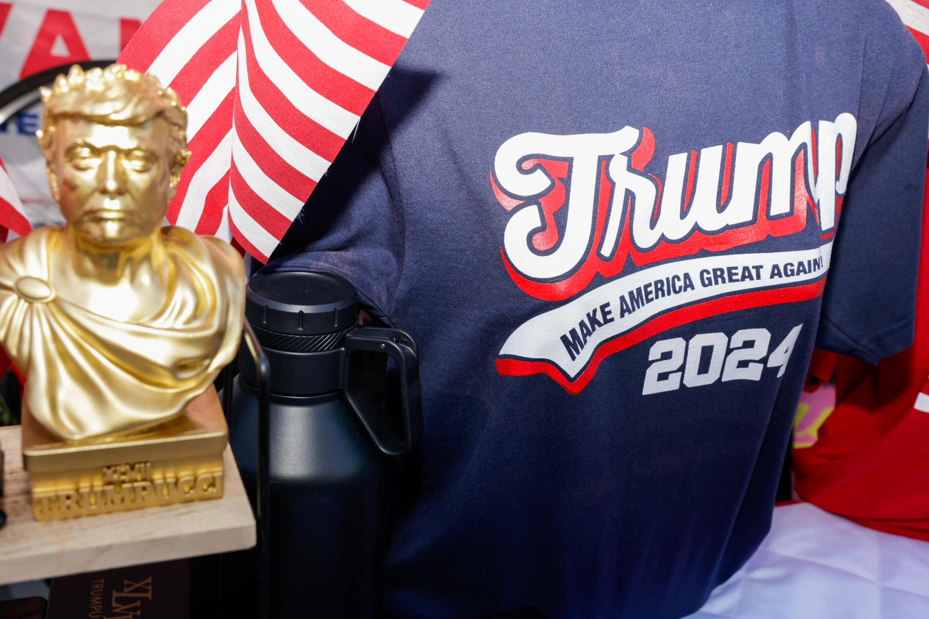 A gold bust, an American flag pattern, and a black bottle are alongside a dark blue shirt with &quot;Trump 2024&quot; and &quot;Make America Great Again&quot; in bold letters.