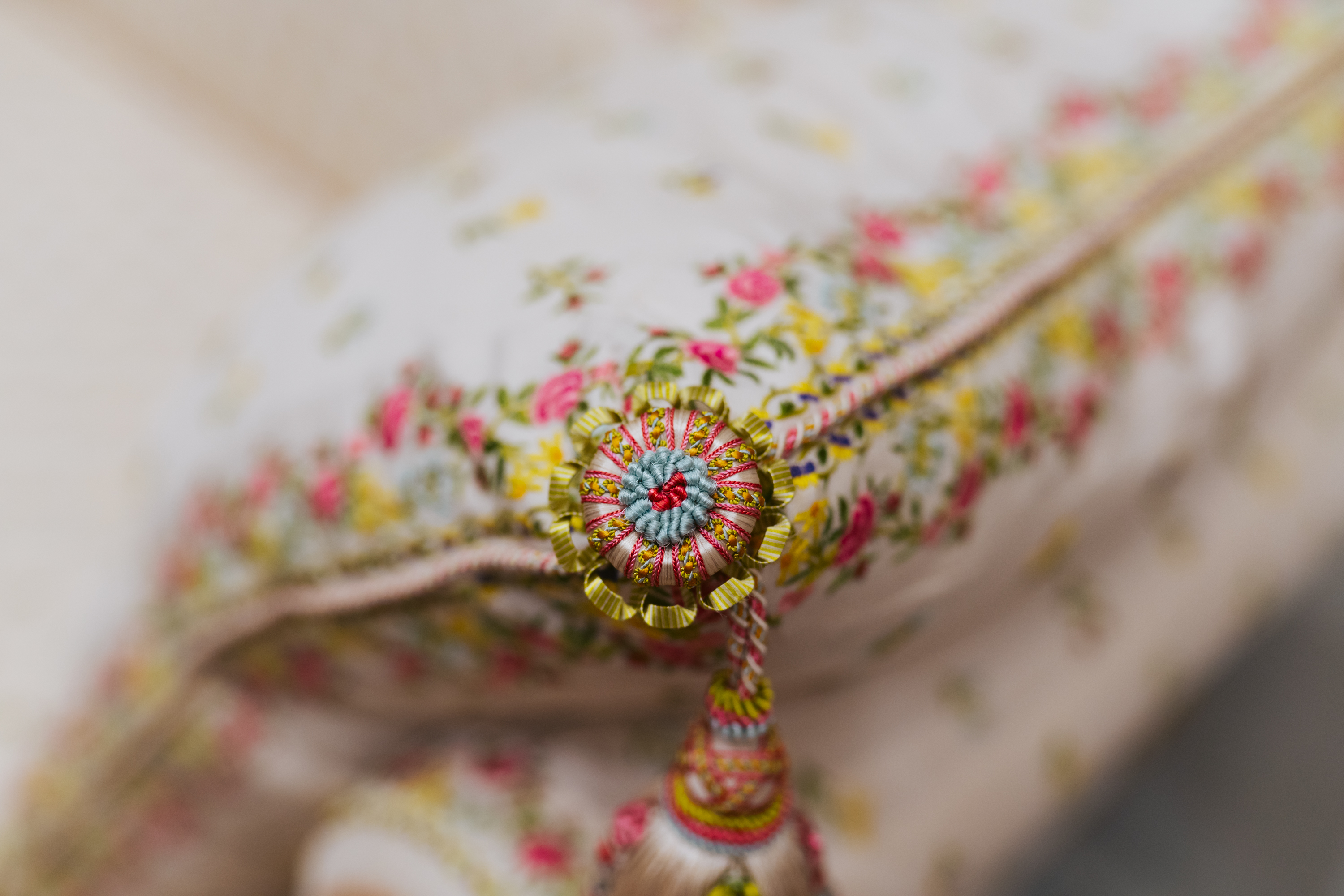 A close-up of a floral-patterned pillow with a decorative button and tassel. The fabric features colorful flowers, primarily pink and yellow.