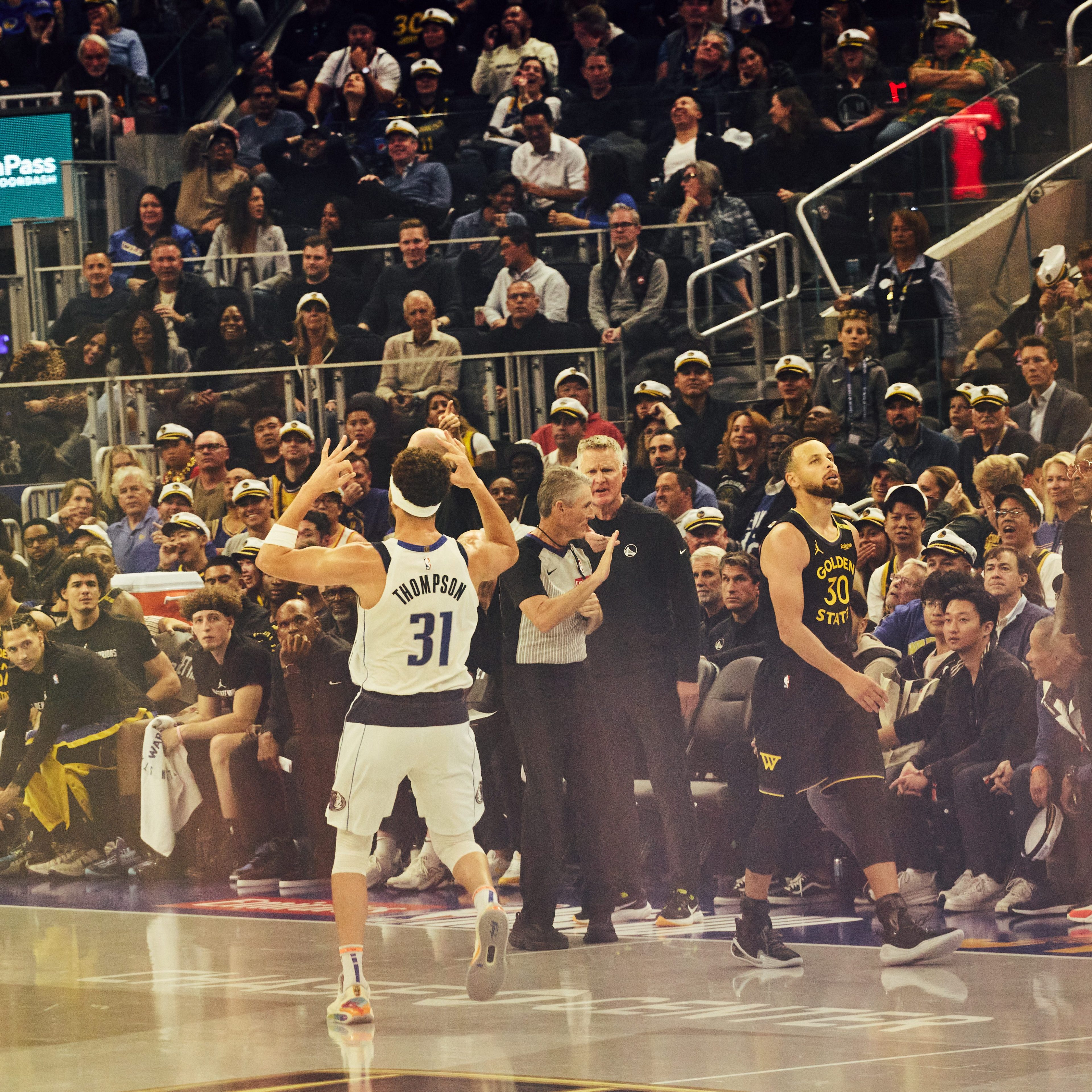 A basketball player named Thompson gestures on the court as another player and fans in the arena watch intensely from the sidelines and stands.