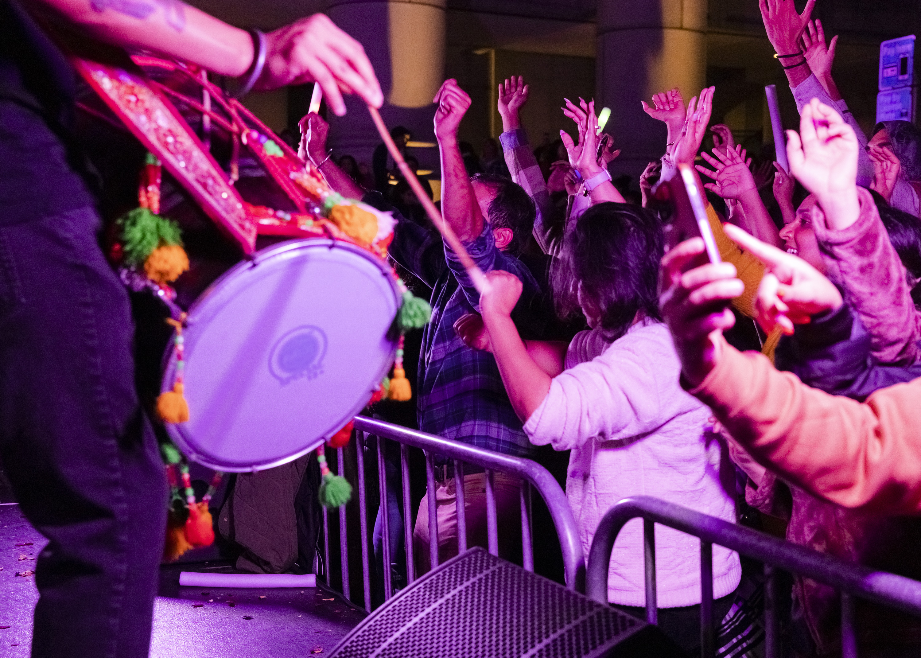 A vibrant scene shows a musician playing a colorful drum as an enthusiastic crowd raises their hands and enjoys the lively atmosphere.