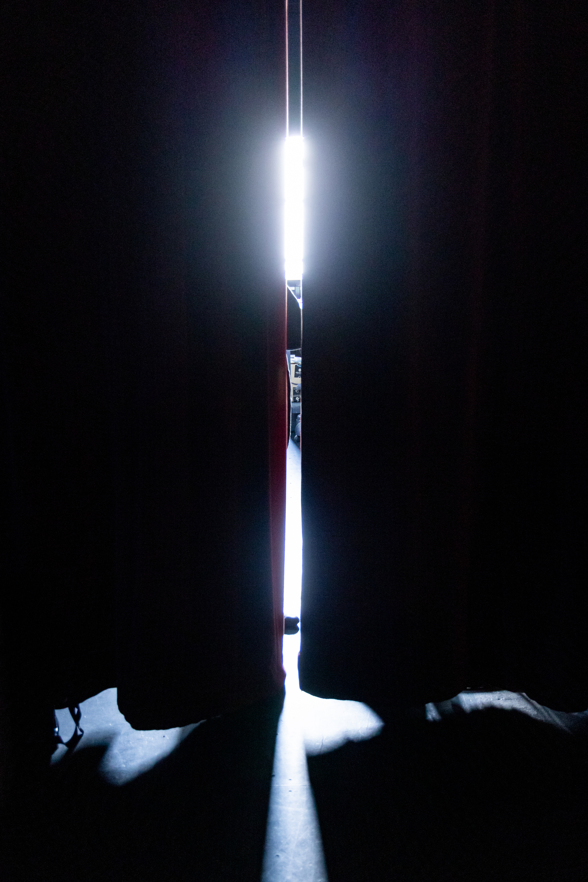 A narrow beam of light breaks through a slight gap between two dark curtains, casting faint shadows on the floor.