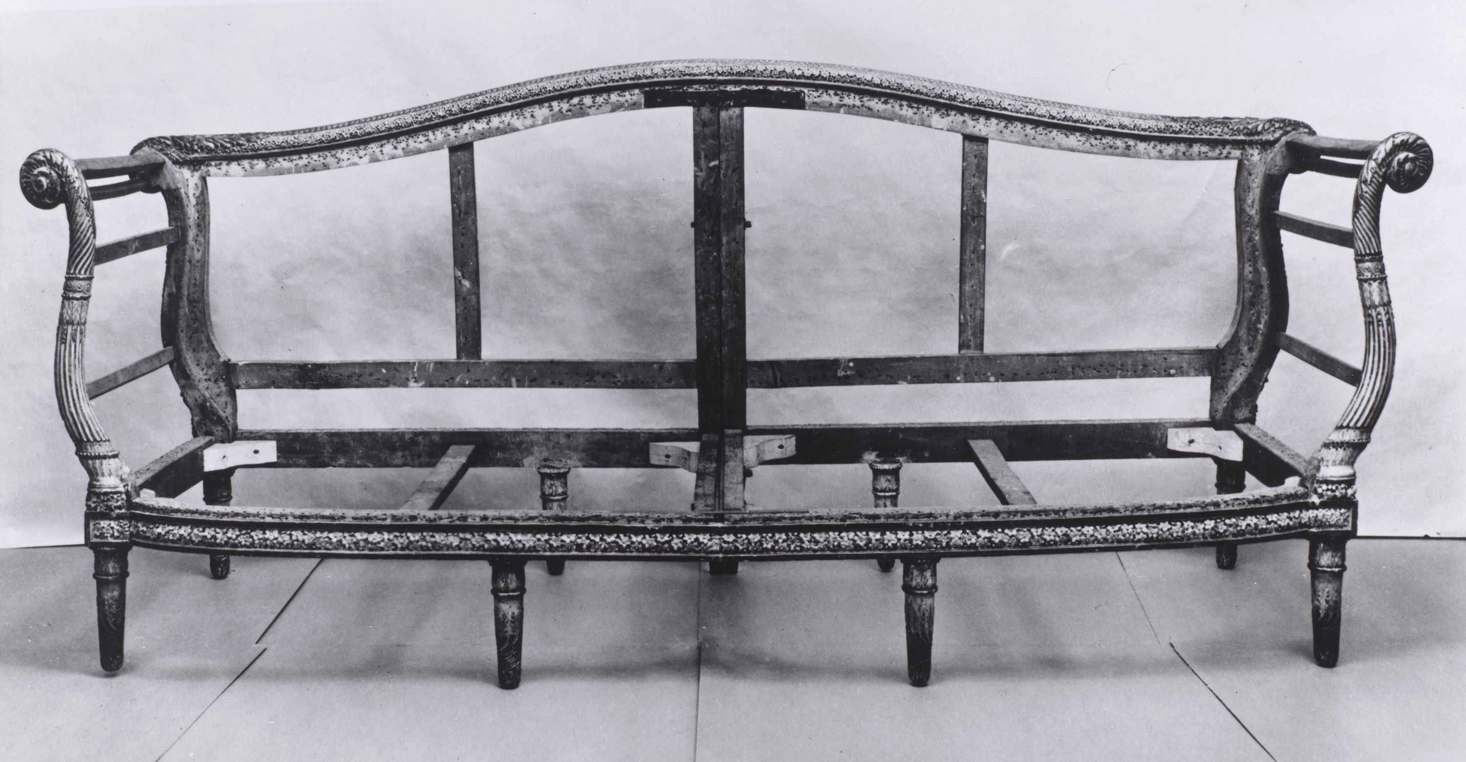 The image shows a vintage wooden sofa frame with ornate carvings and curved arms. It lacks upholstery, exposing the structure and design details.