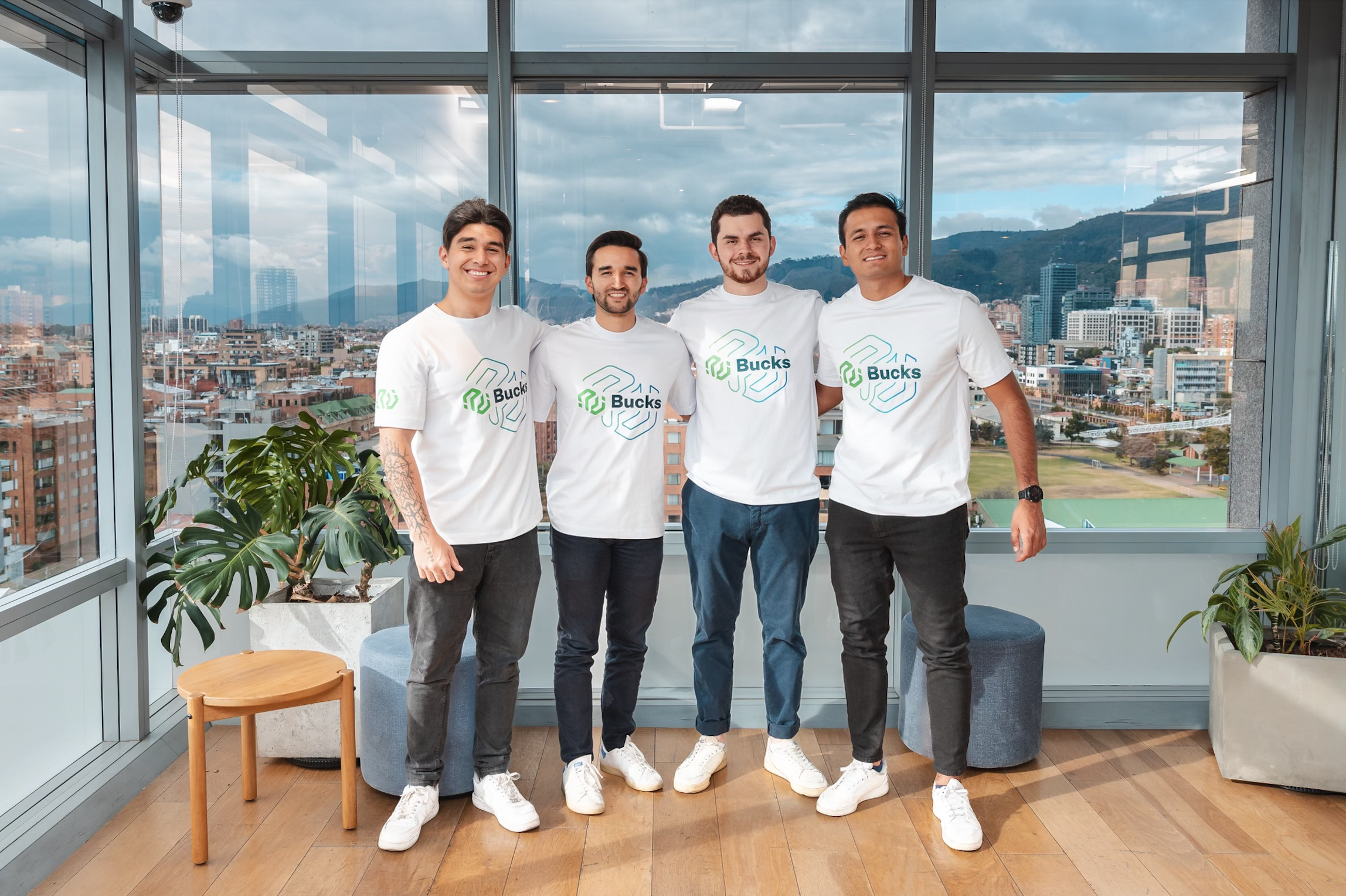 Four men stand together in an office in matching white shirts and jeans.