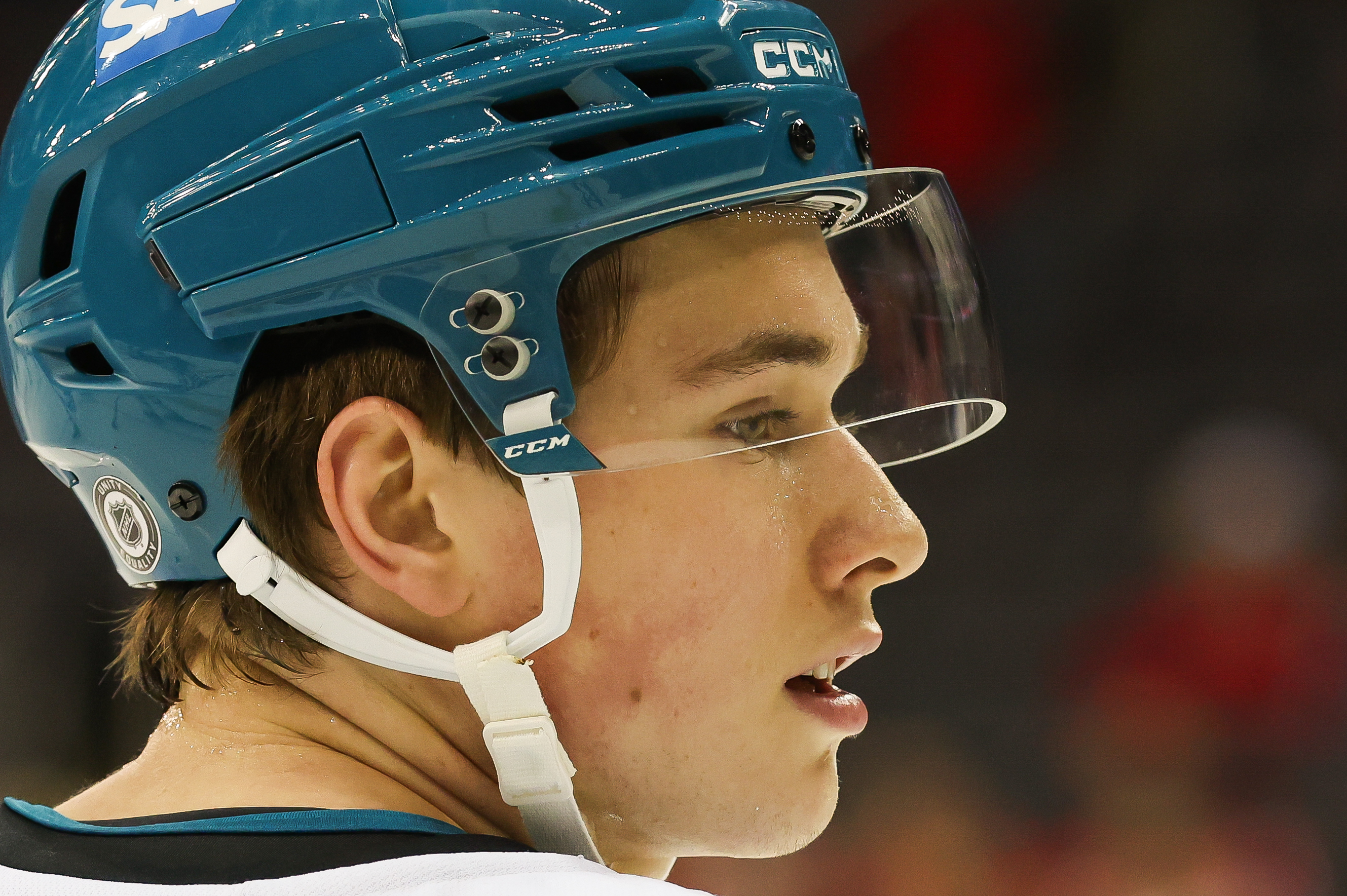 A young hockey player is shown in profile, focused and wearing a teal helmet with a clear visor. Subtle details like the logo and helmet brand are visible.