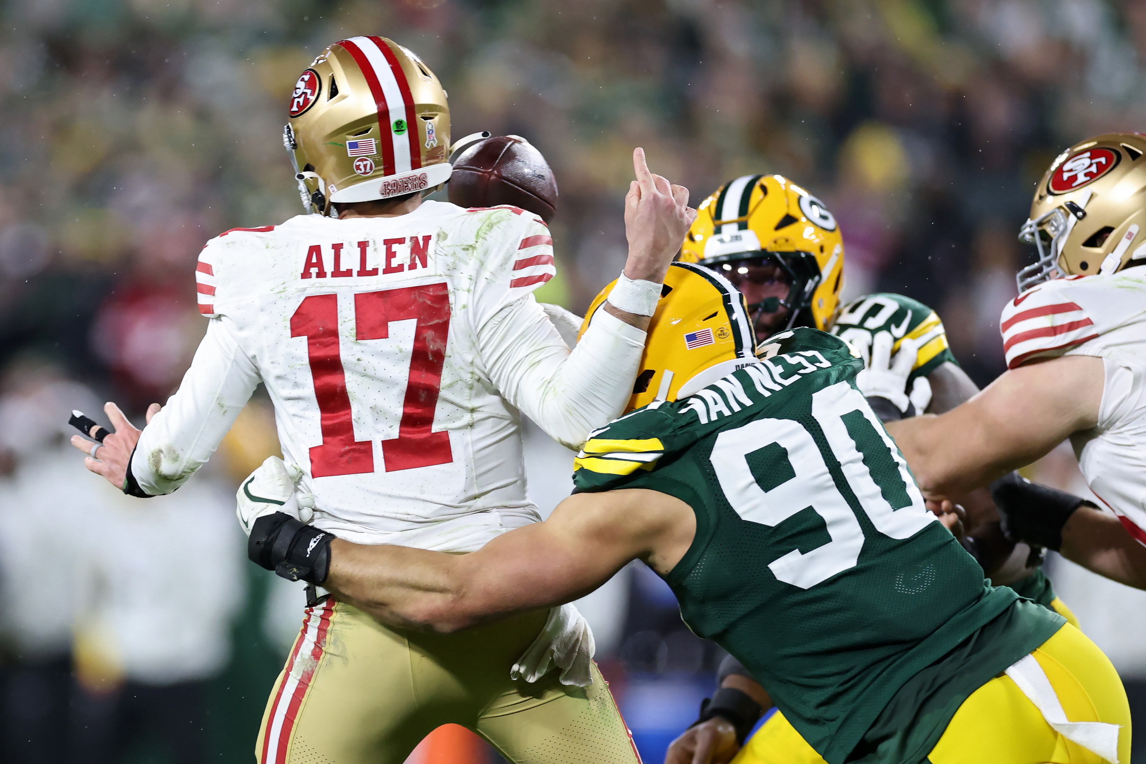 A football player in a white jersey, number 17, is being tackled by a player in a green jersey, number 90. The scene is intense and action-packed.