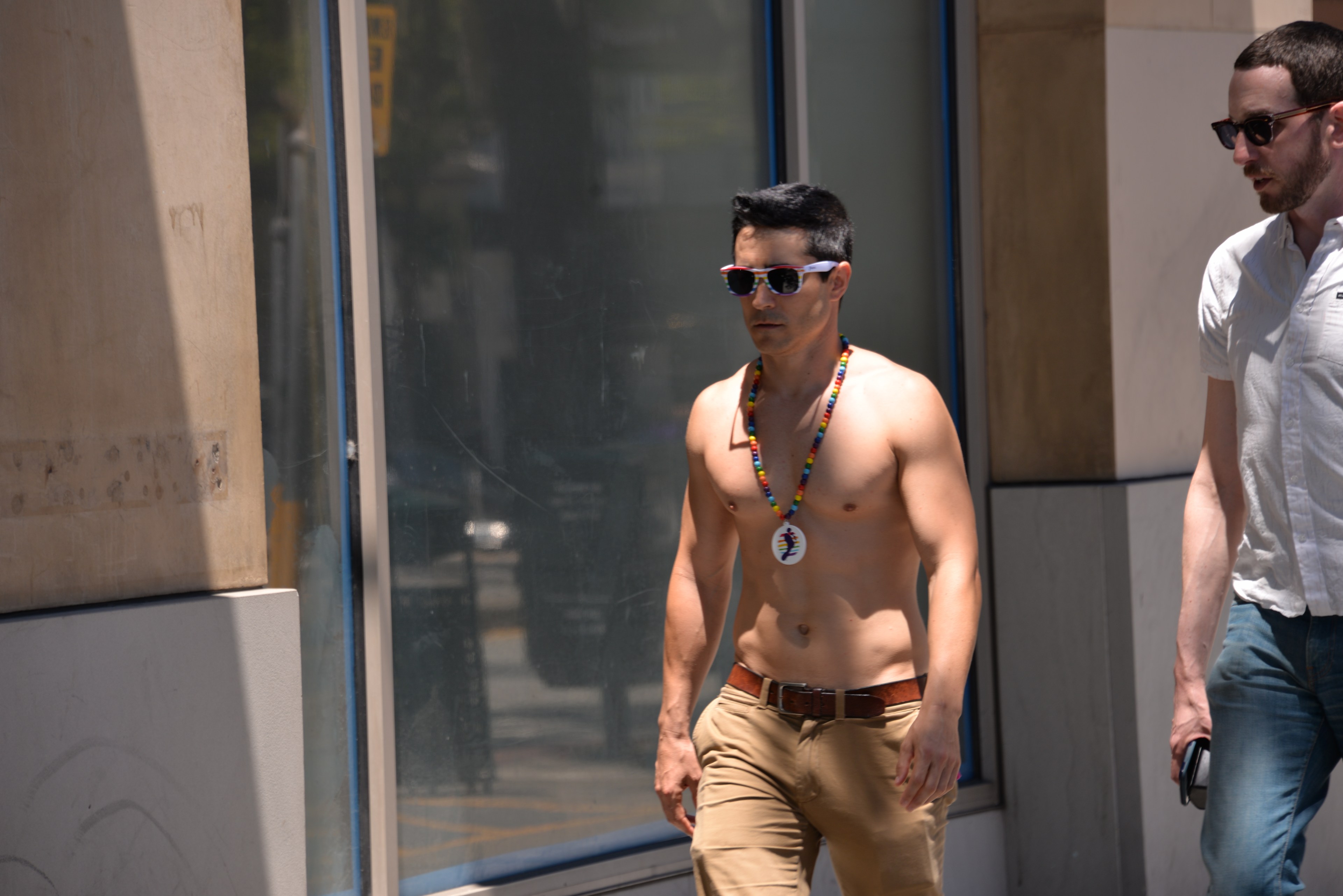 Johnston is shirtless and wearing khaki pants as he walks down a street wearing sunglasses.