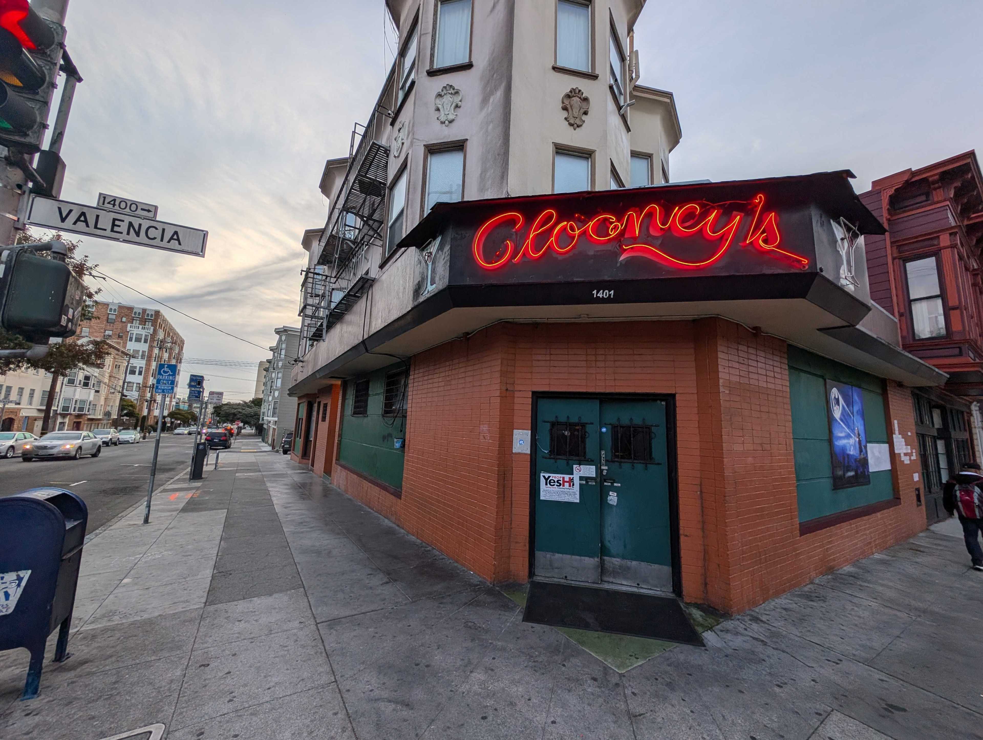 The image shows a street corner with a building featuring a red neon sign reading &quot;Clooney's.&quot; A &quot;Valencia&quot; street sign and cars are visible.