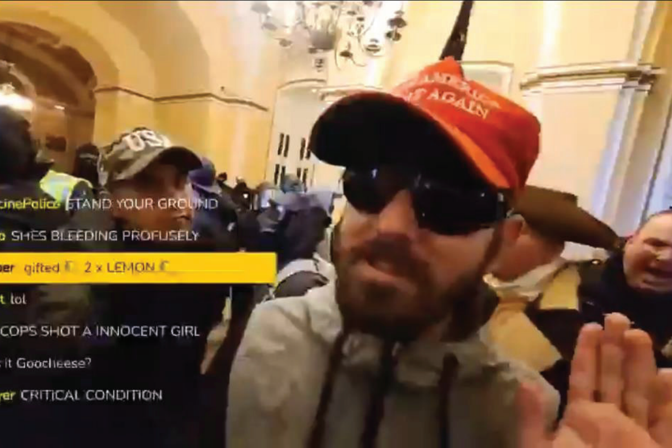 A man in sunglasses and a red hat is in a crowded room with people wearing hats and masks. There's a live chat overlay on the left.