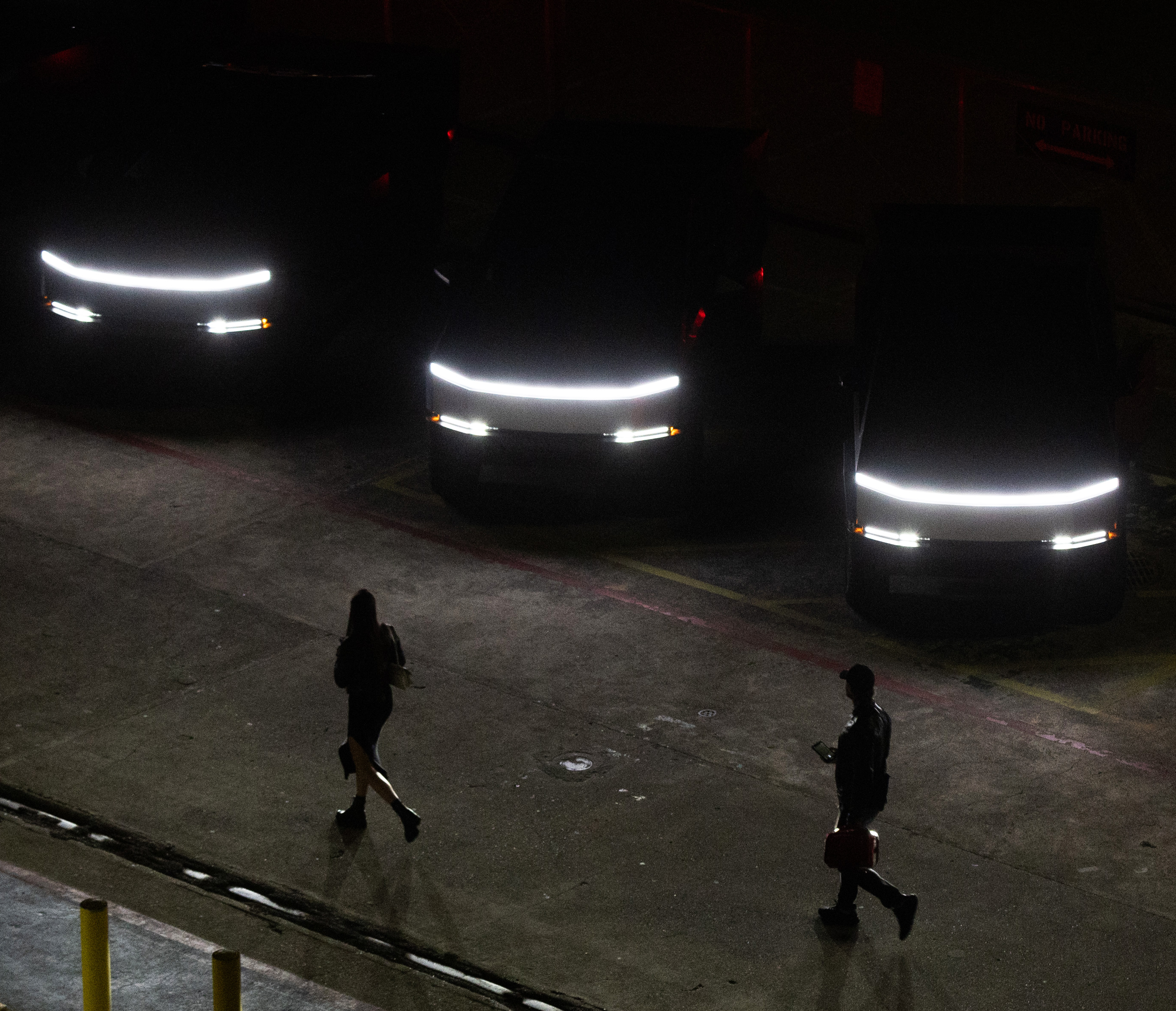 Pedestrians walk past Tesla Cybertrucks’s parked in a line at the SF Deep Tech Week launch party on the USS Hornet aircraft carrier in Alameda on Sunday, June 23, 2024. The event includes tech showcases, demos and a rave. The USS Hornet is retired and operates as a sea, air and space museum.