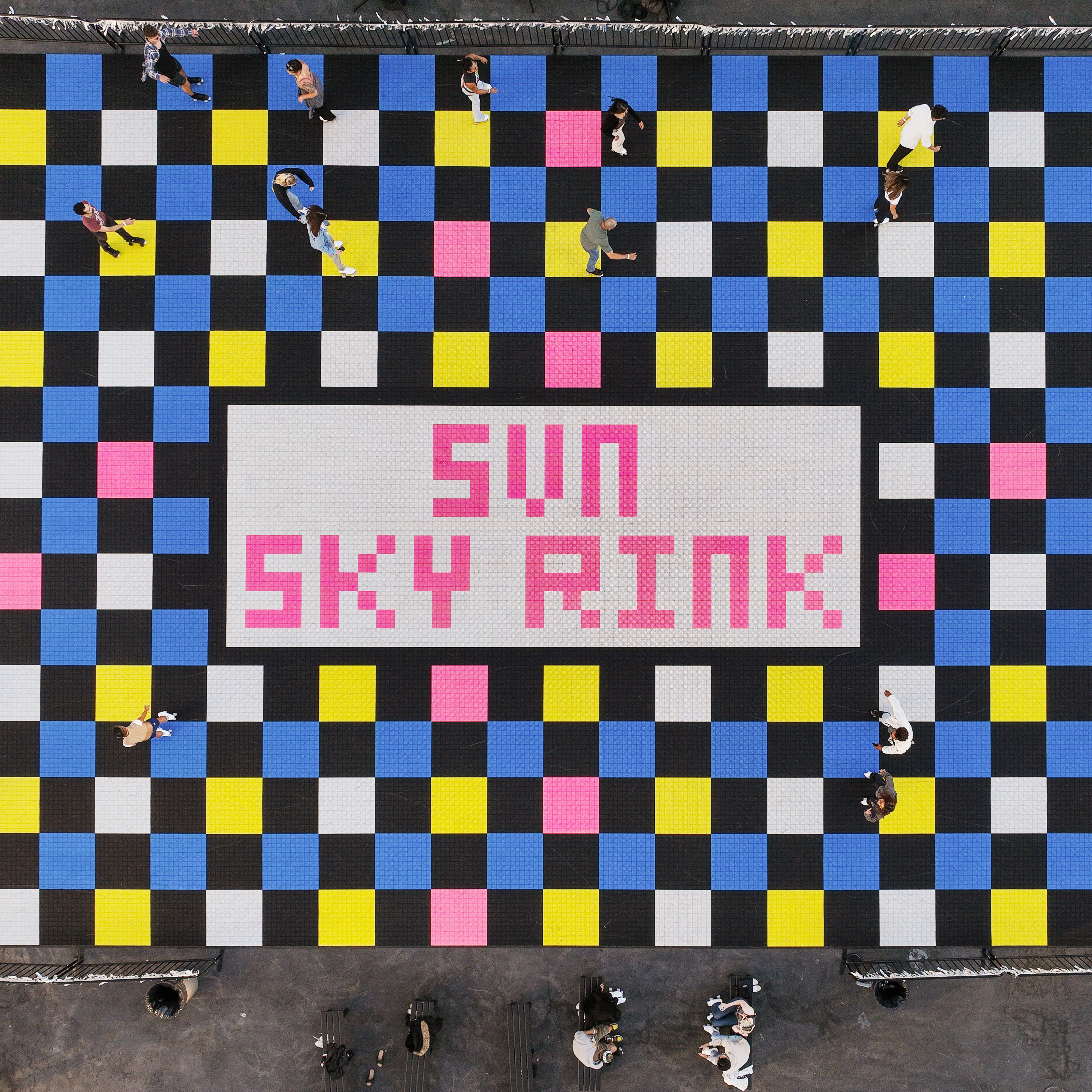 The image shows a colorful checkered floor with people walking on it. The center has a white rectangle with &quot;SUN SKY RINK&quot; written in pink letters.