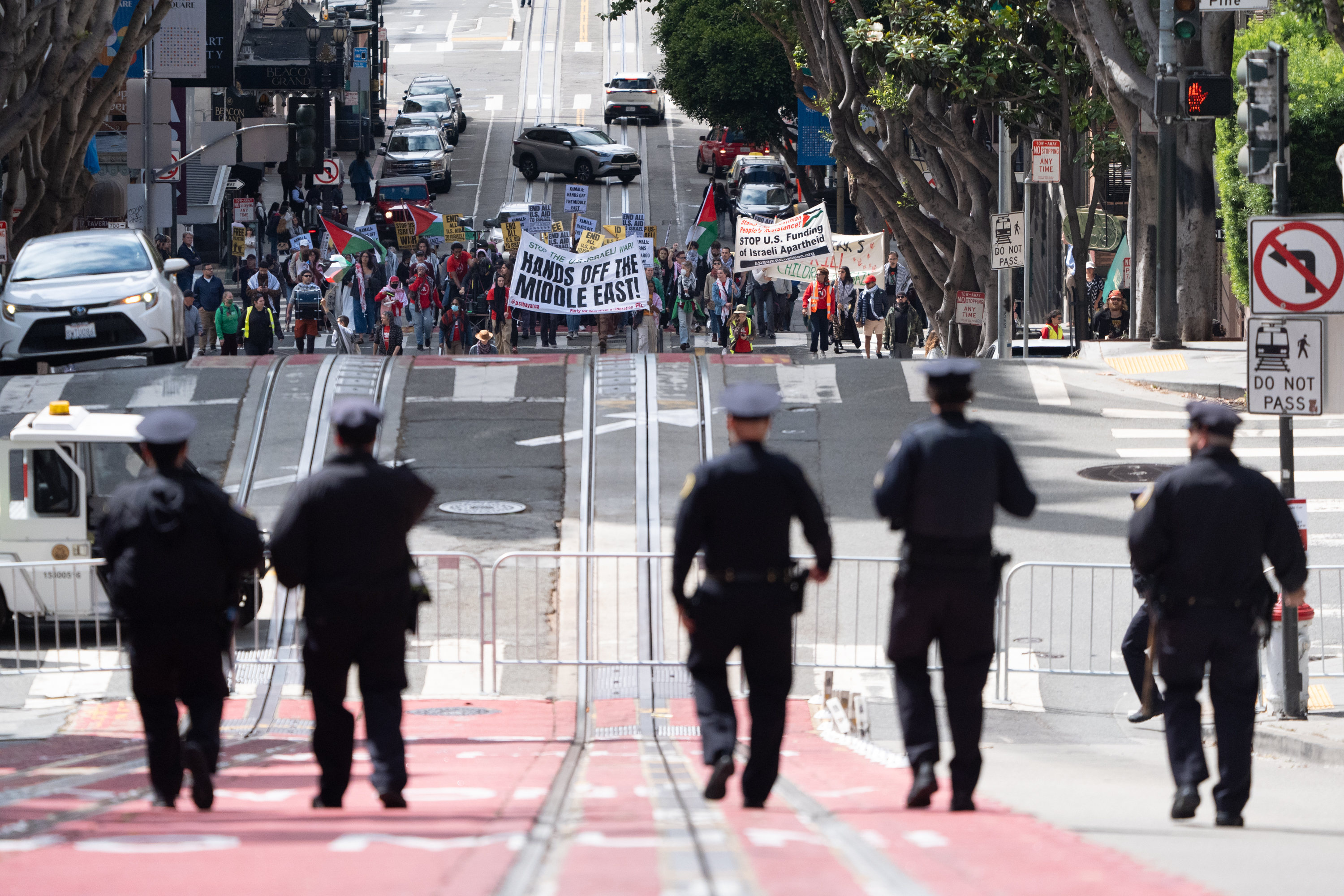 A crowd of protesters holds signs and banners, such as &quot;Hands off the Middle East,&quot; marching up a city street. Police officers stand in the foreground.