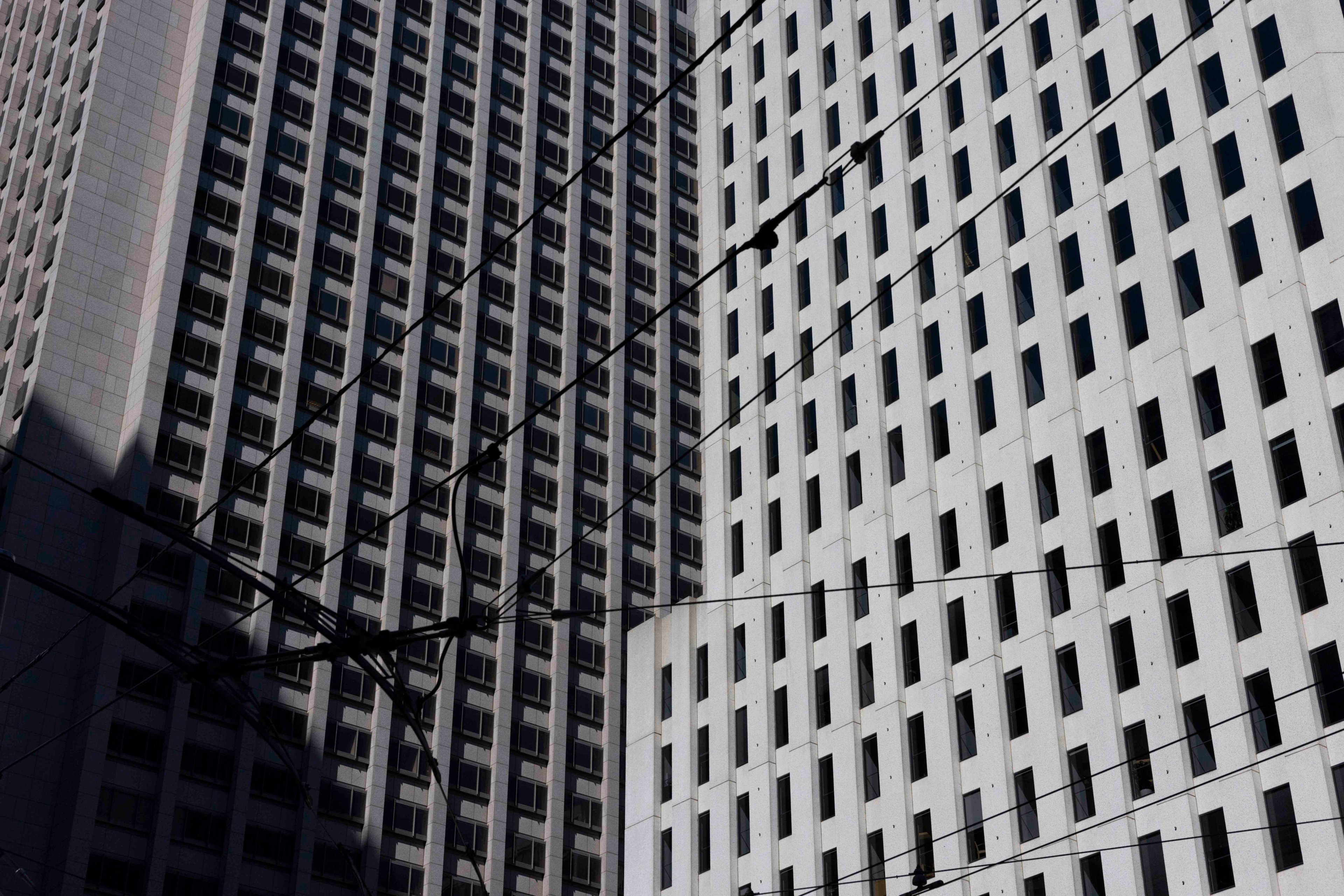 The image shows two tall, grid-patterned skyscrapers intersected by numerous overhead power lines. The buildings are closely aligned, creating an urban scene.