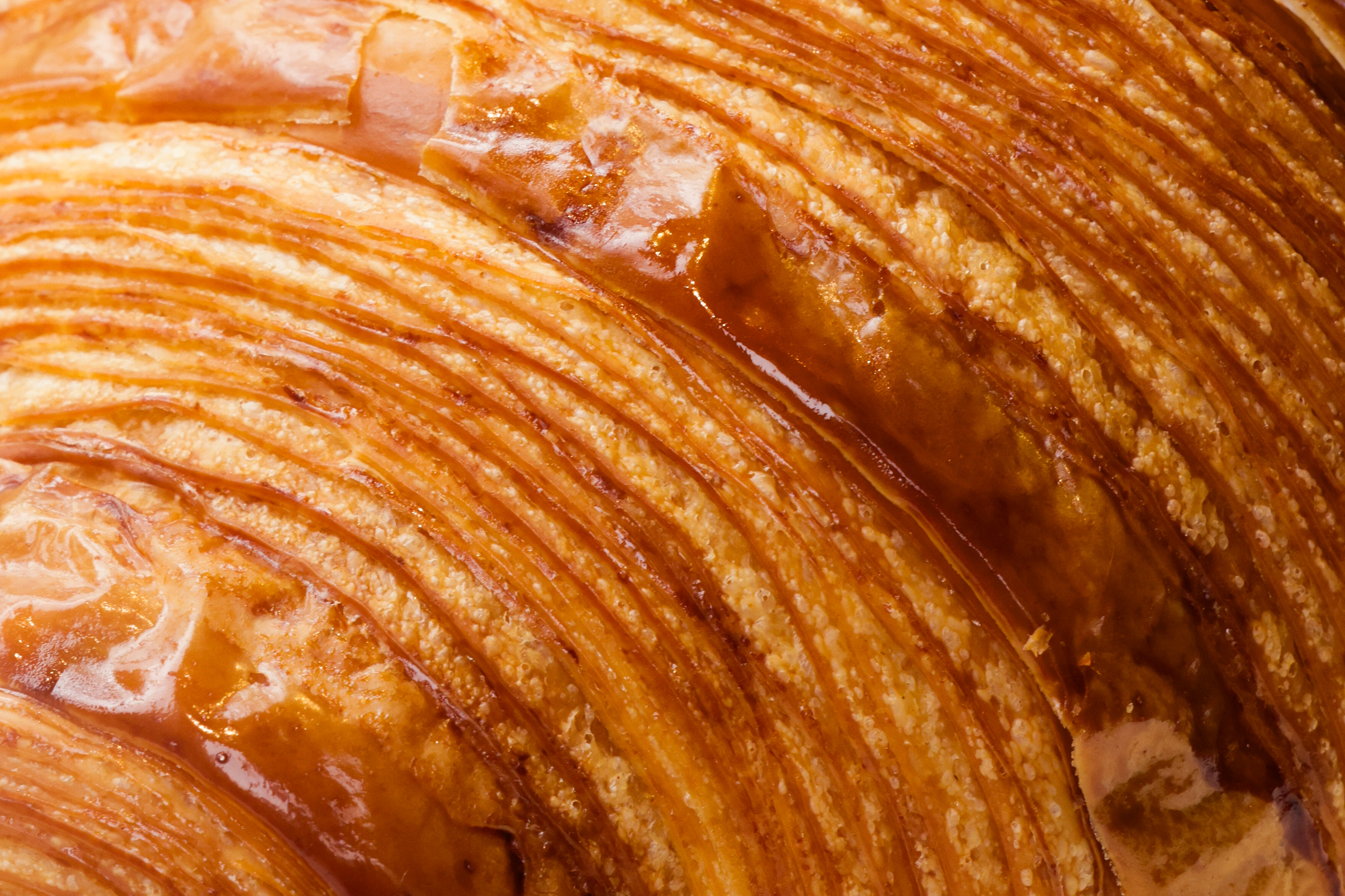 The image shows a close-up of a flaky, golden-brown pastry with shiny, crisp layers, indicating a freshly baked, buttery texture.