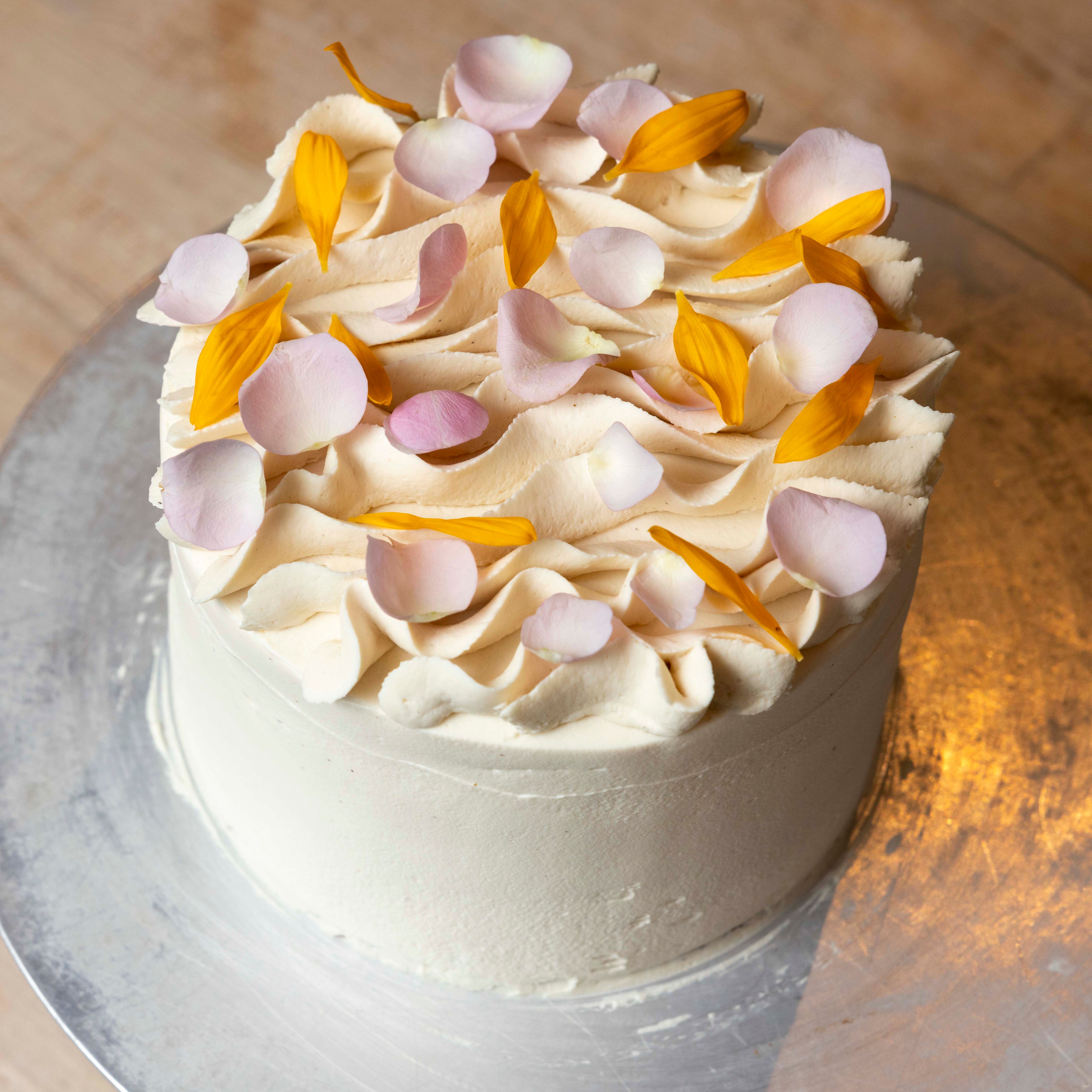 A cake with smooth white frosting is adorned with delicate pink and yellow flower petals arranged artistically on top.