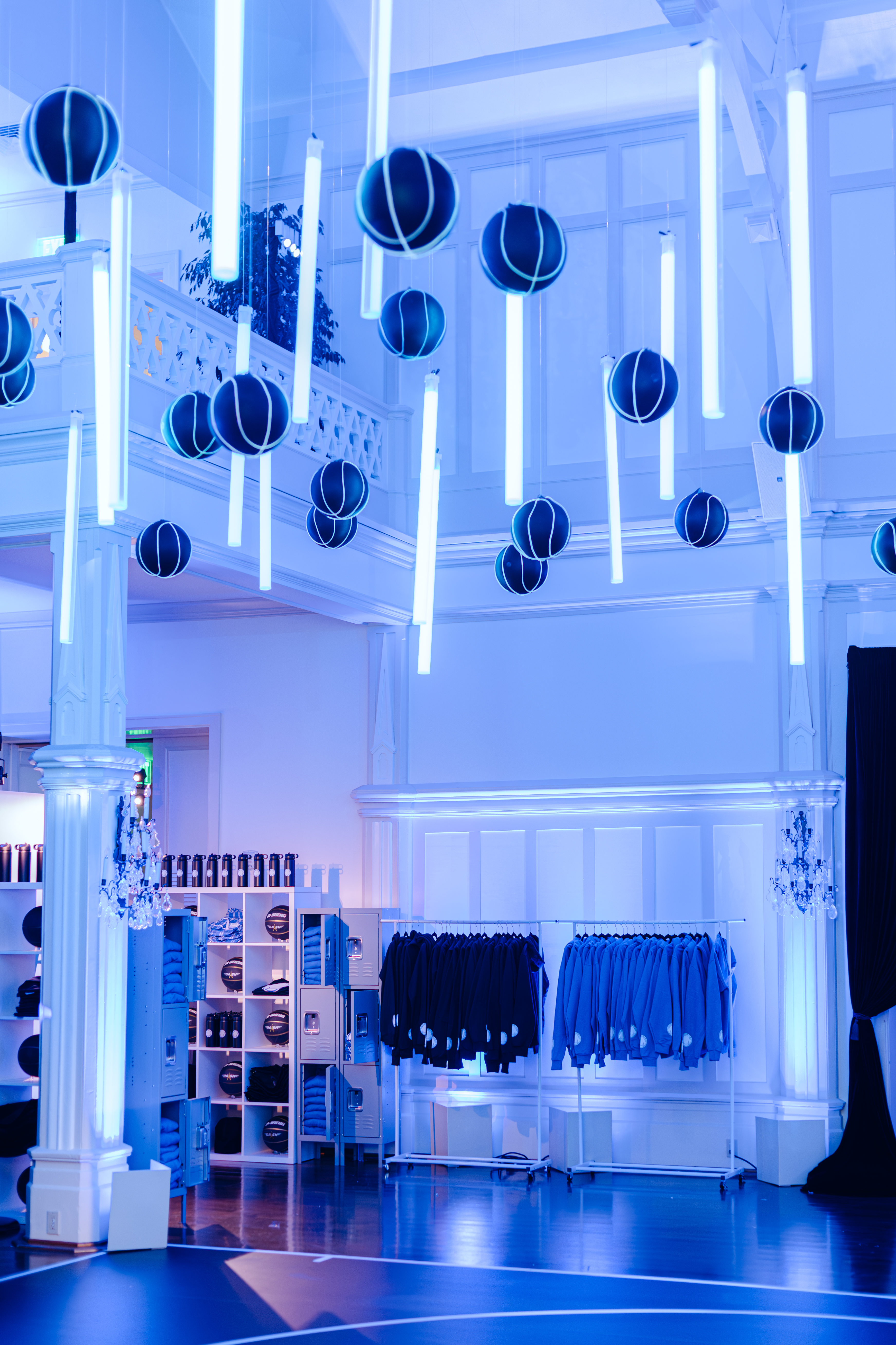 The image shows a futuristic room with blue lighting, hanging cylindrical lights and black spherical decorations, clothing racks, and shelves with folded apparel.