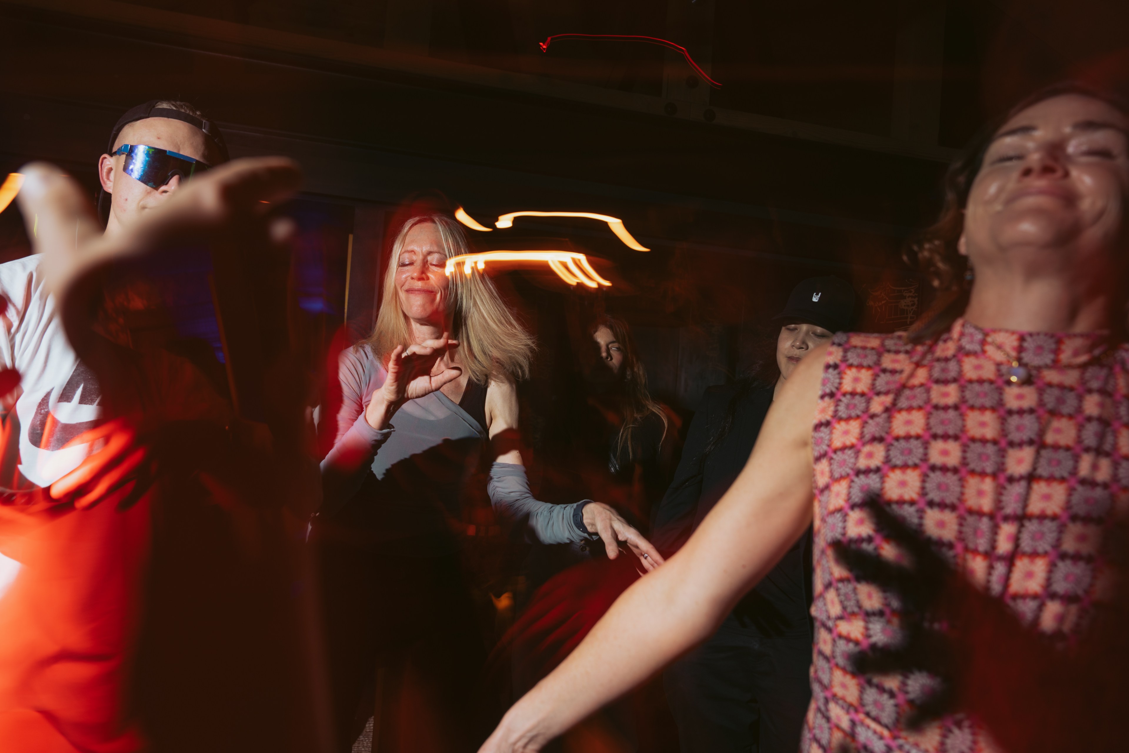 People are dancing energetically in a dimly lit space, with red and warm light trails enhancing the lively atmosphere.