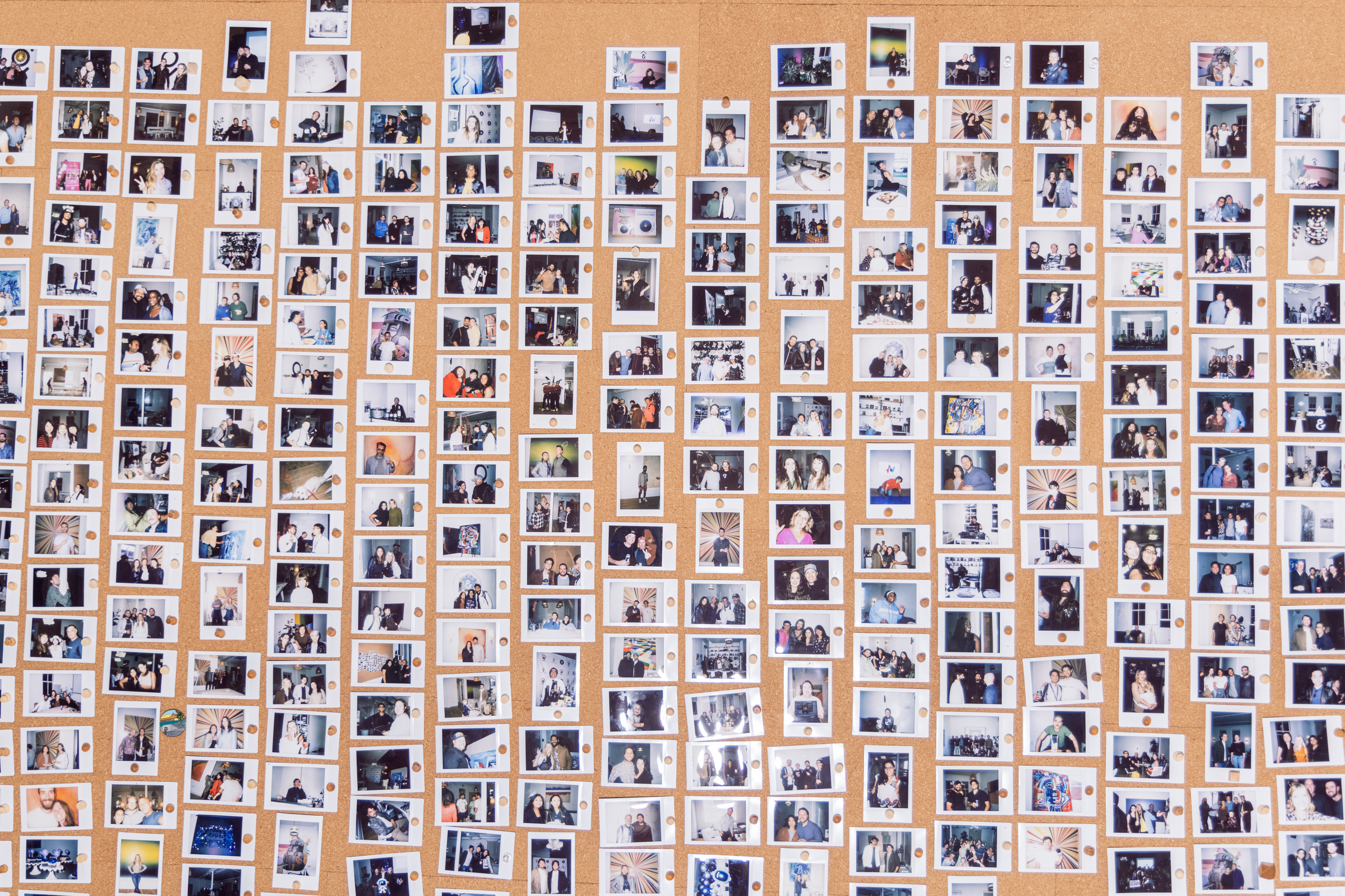 A corkboard filled with numerous Polaroid photos depicting groups of people, each pinned neatly in rows, showcasing various scenes and moments.