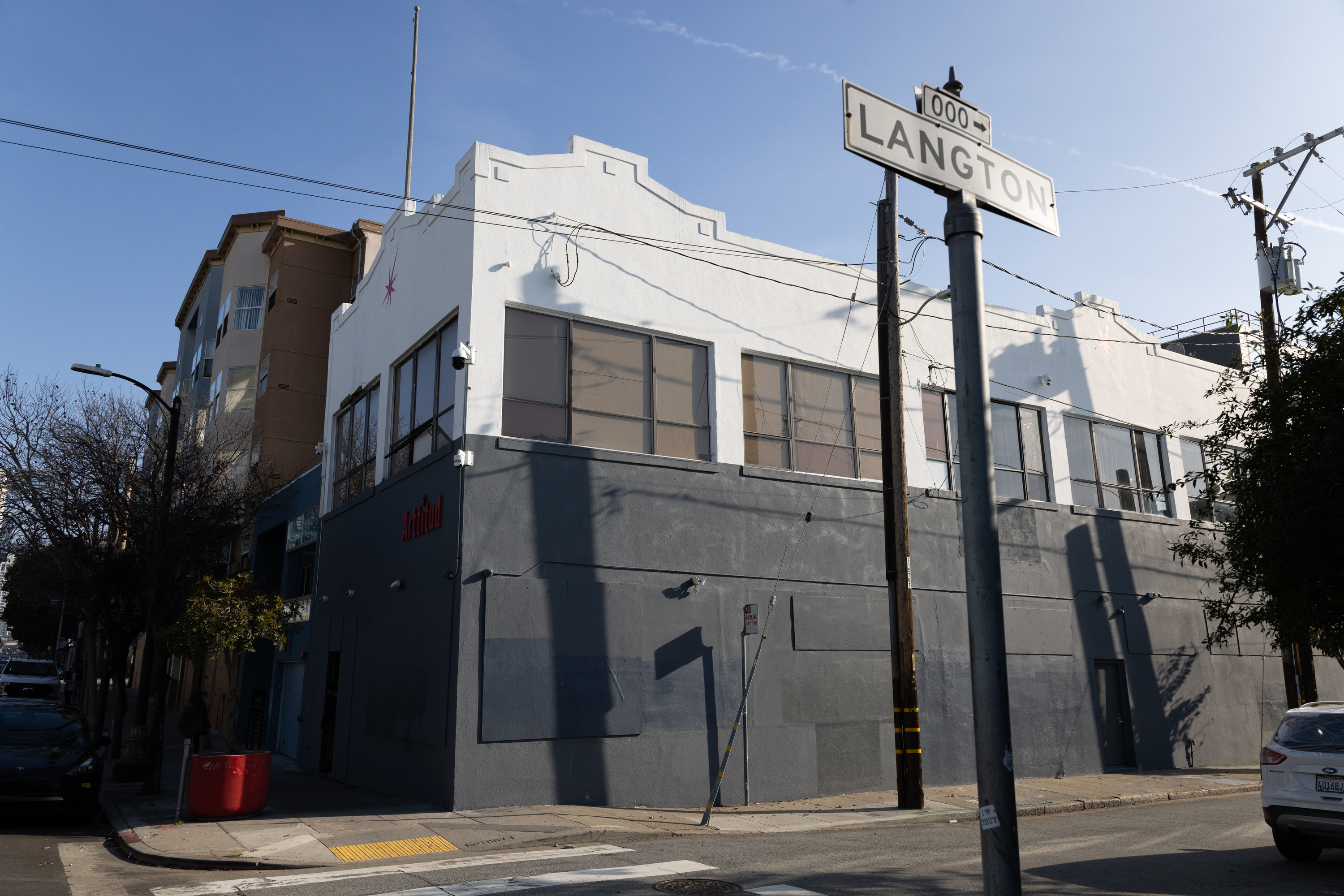 The image shows a two-story building on a street corner with a white upper facade and gray lower section. There's a street sign reading &quot;LANGTON&quot; in the foreground.