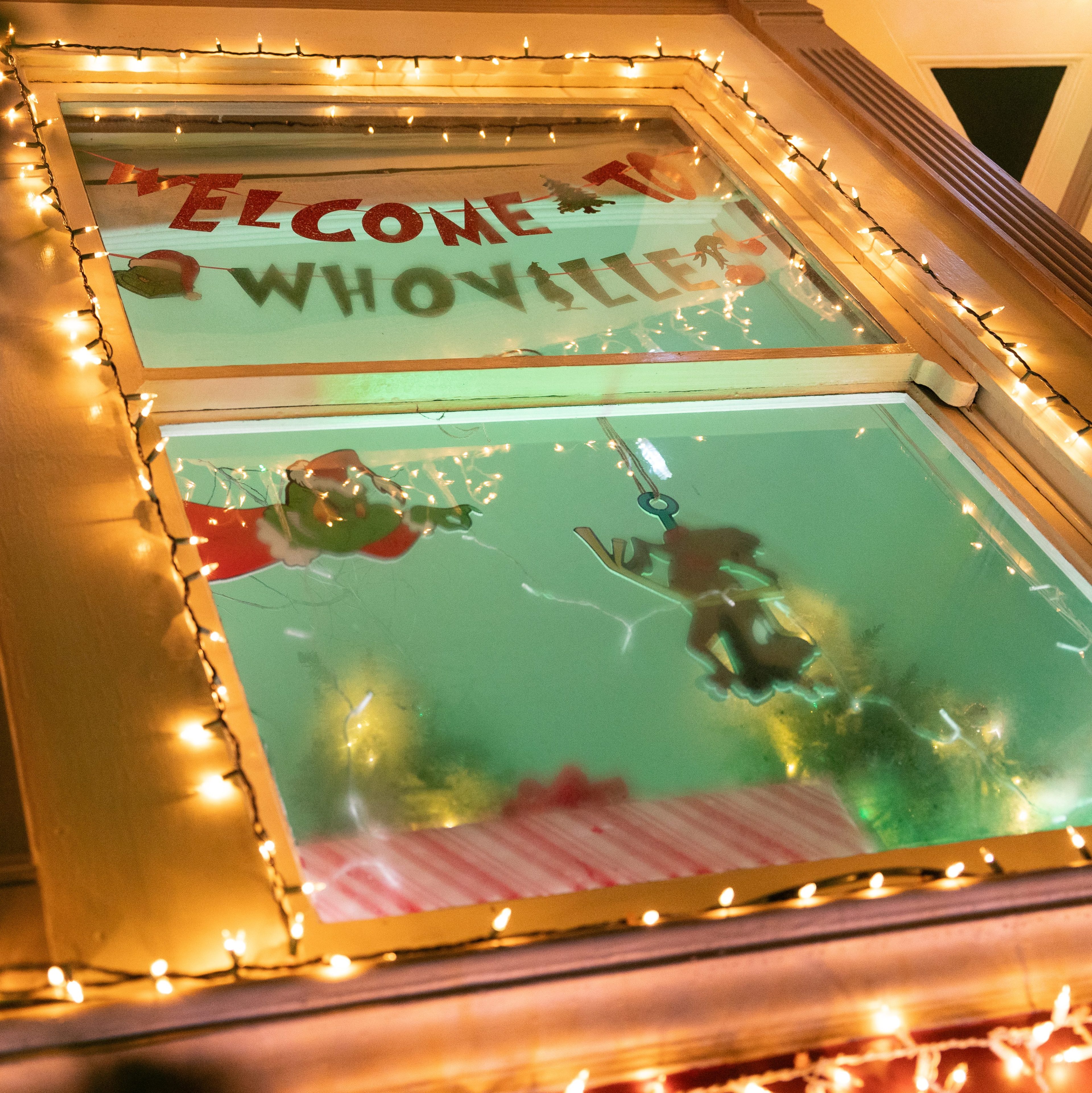 A window decorated with string lights and a sign saying &quot;Welcome to Whoville&quot; with Christmas-themed cutouts, likely inspired by Dr. Seuss.