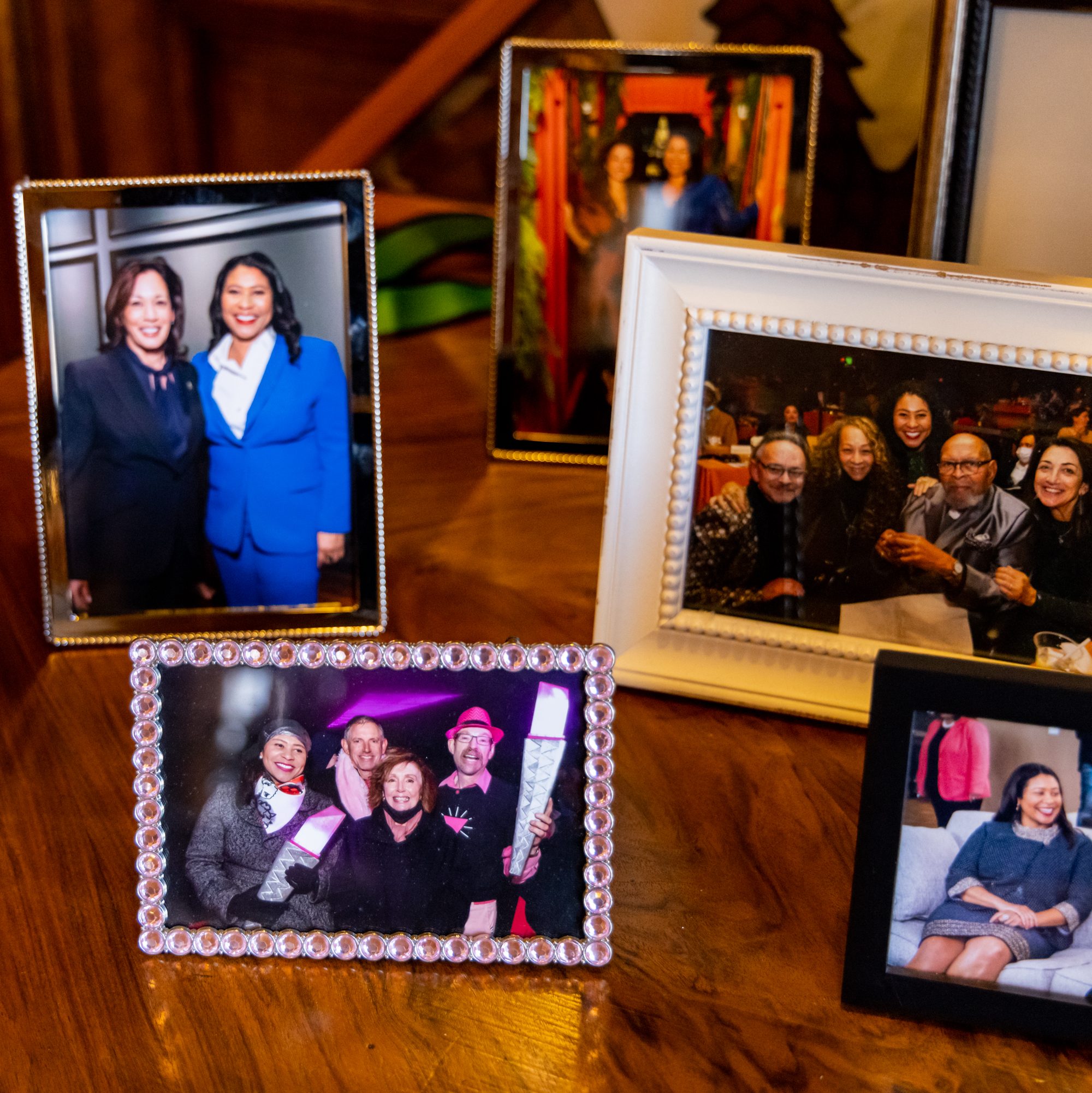 This image shows several framed photos of people smiling in various settings, displayed on a wooden surface. The frames are of different styles and sizes.