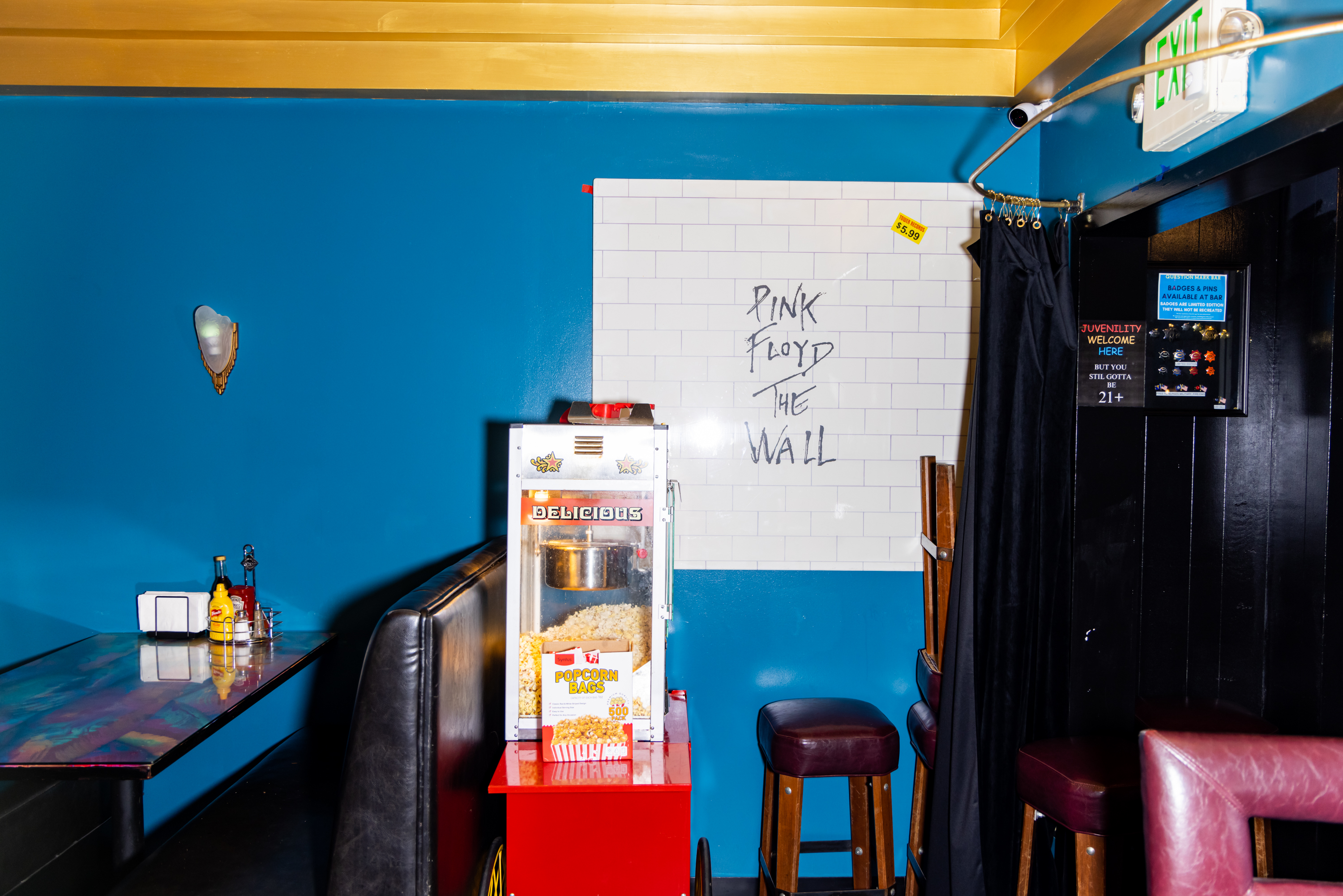 The image shows a vibrant room with a blue wall, a popcorn machine, and a sign reading &quot;Pink Floyd The Wall.&quot; A booth with condiments is visible on the left.