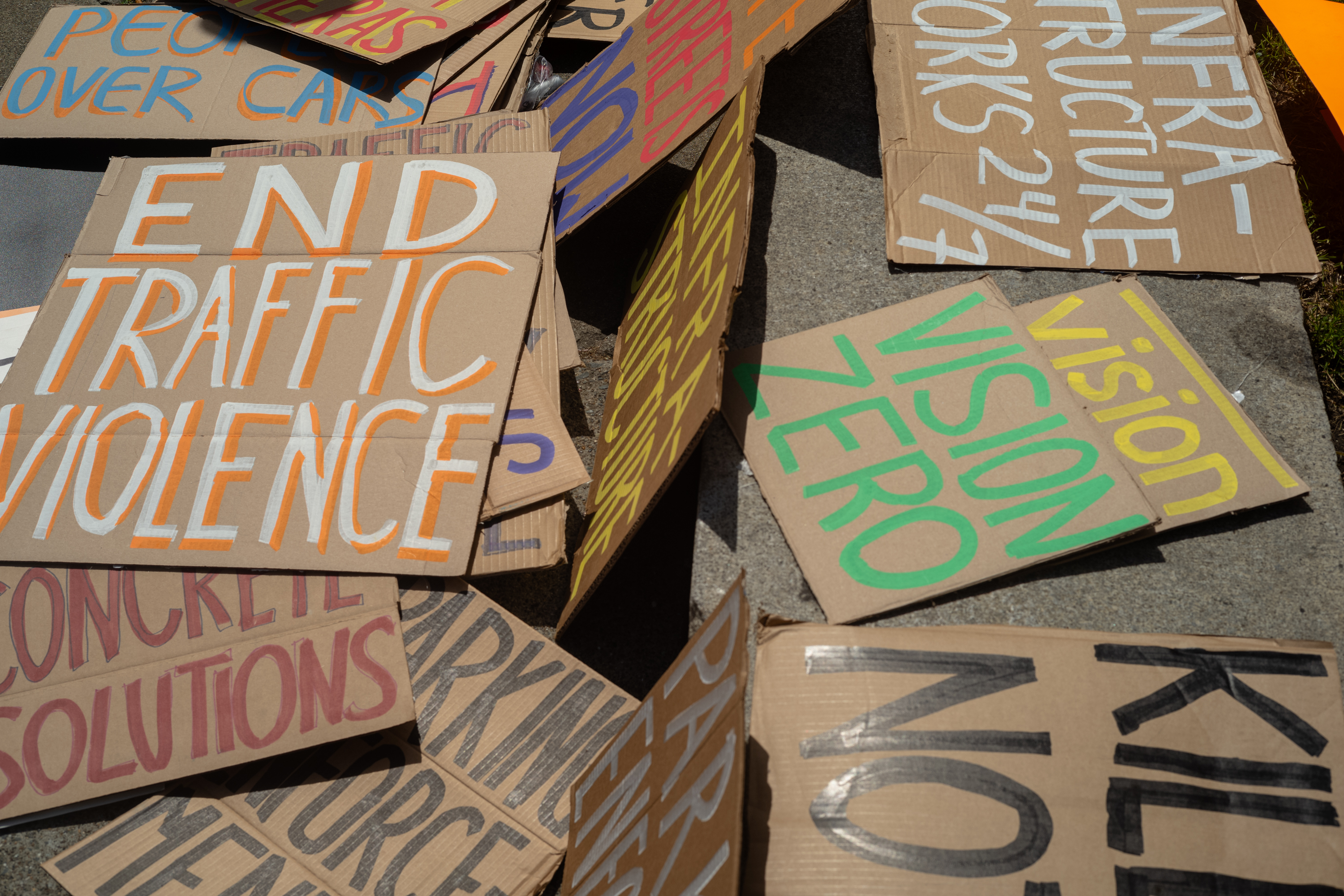 The image shows several cardboard protest signs with messages like &quot;END TRAFFIC VIOLENCE&quot; and &quot;VISION ZERO,&quot; emphasizing safety and infrastructure improvement.