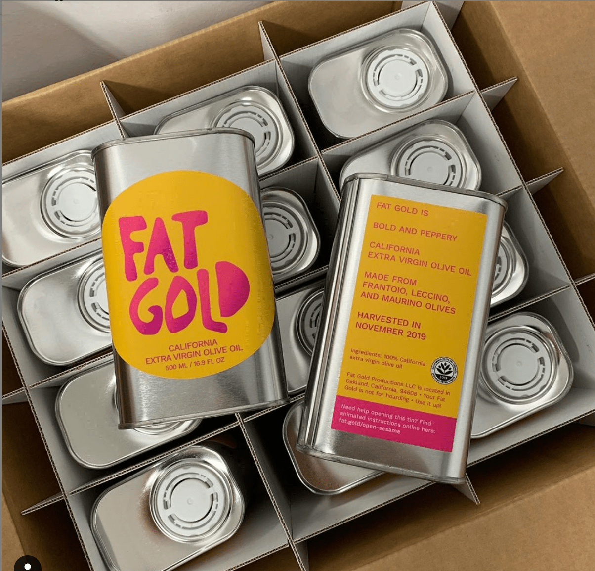 The image shows tins of &quot;Fat Gold&quot; California extra virgin olive oil in a box. The label mentions the oil is bold and peppery, made from various olive types.