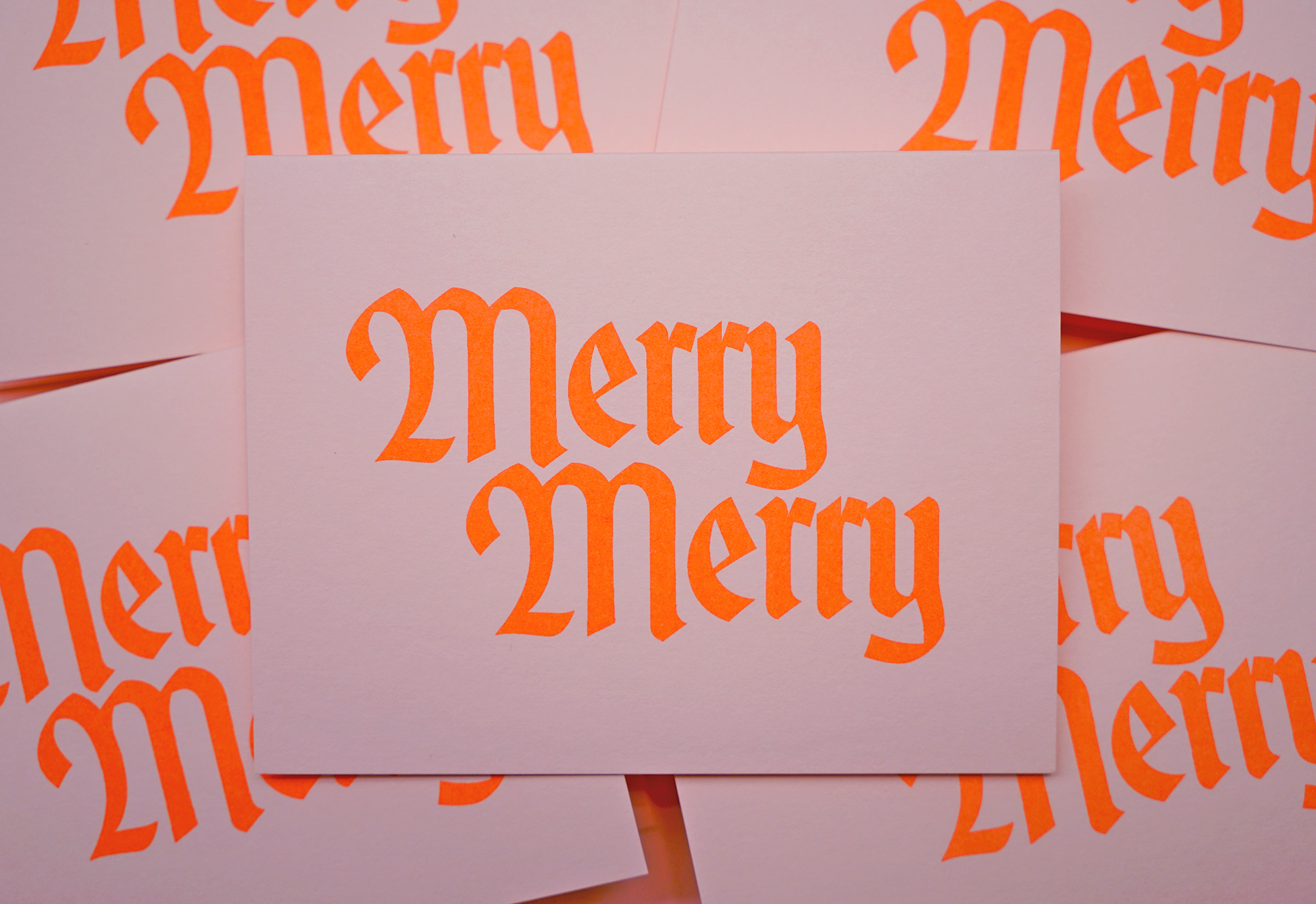 A card with &quot;Merry Merry&quot; printed in bright orange, Gothic-style letters is set among similar cards, creating a festive and cheerful atmosphere.