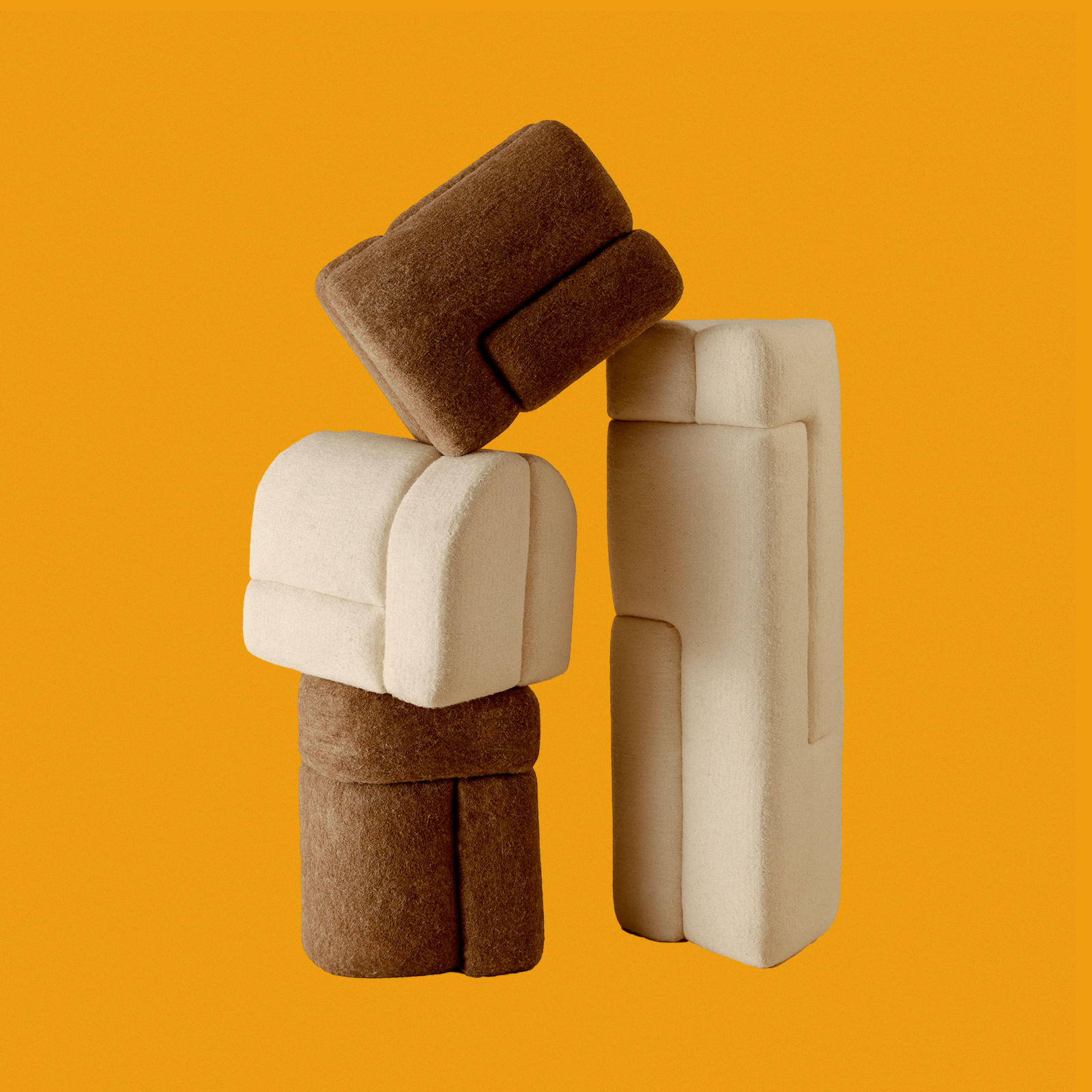 Three plush, abstract shapes are stacked against an orange background, resembling geometric blocks in cream and brown hues.