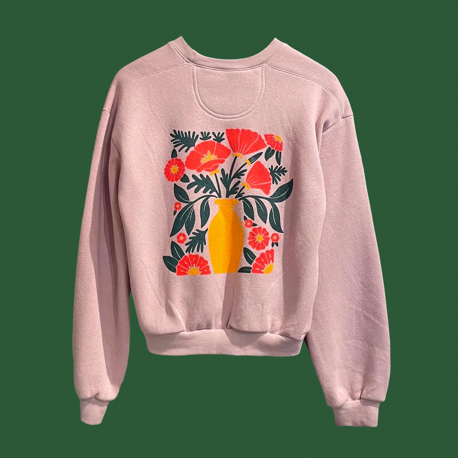 A pink sweatshirt features a colorful graphic of a yellow vase filled with vibrant red flowers and green leaves on the front.