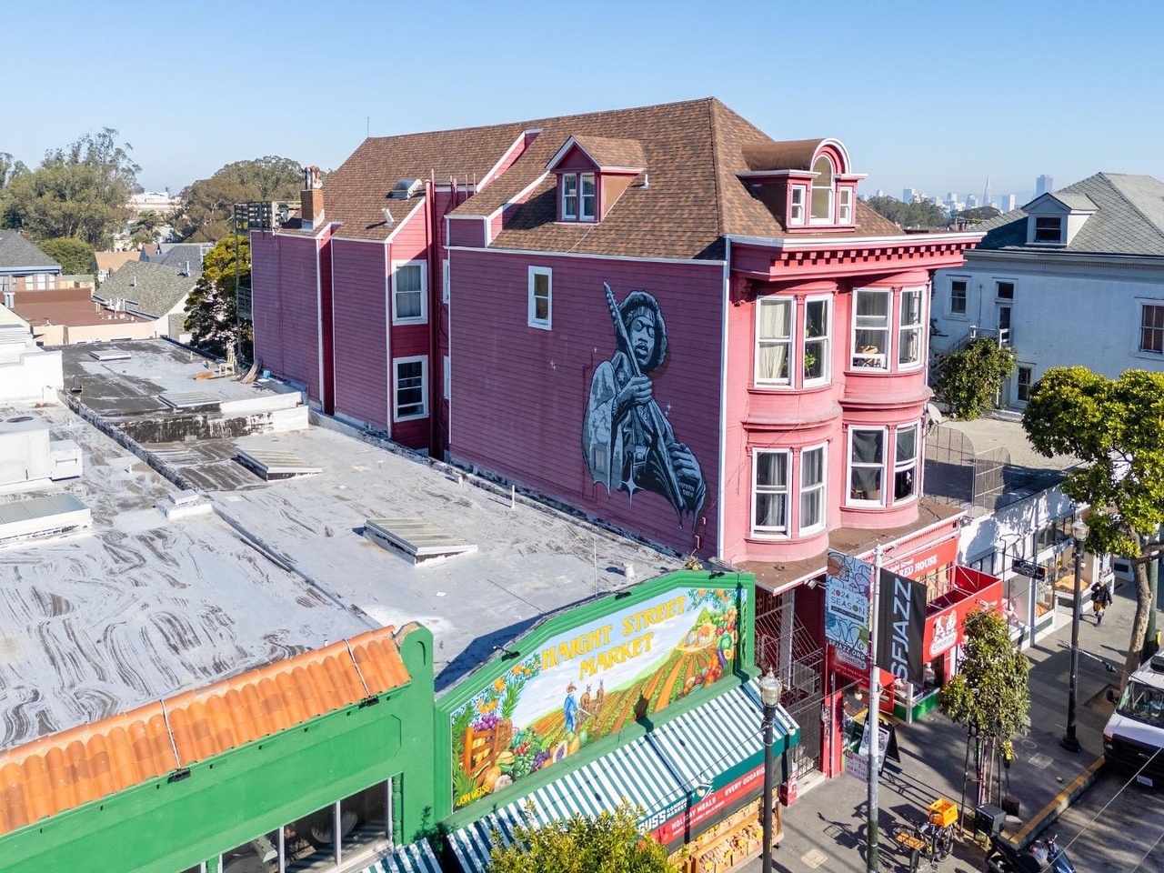 A mural of a musician holding a guitar is painted on a red building. Below, there's a colorful market with a bright striped awning and a few storefronts.