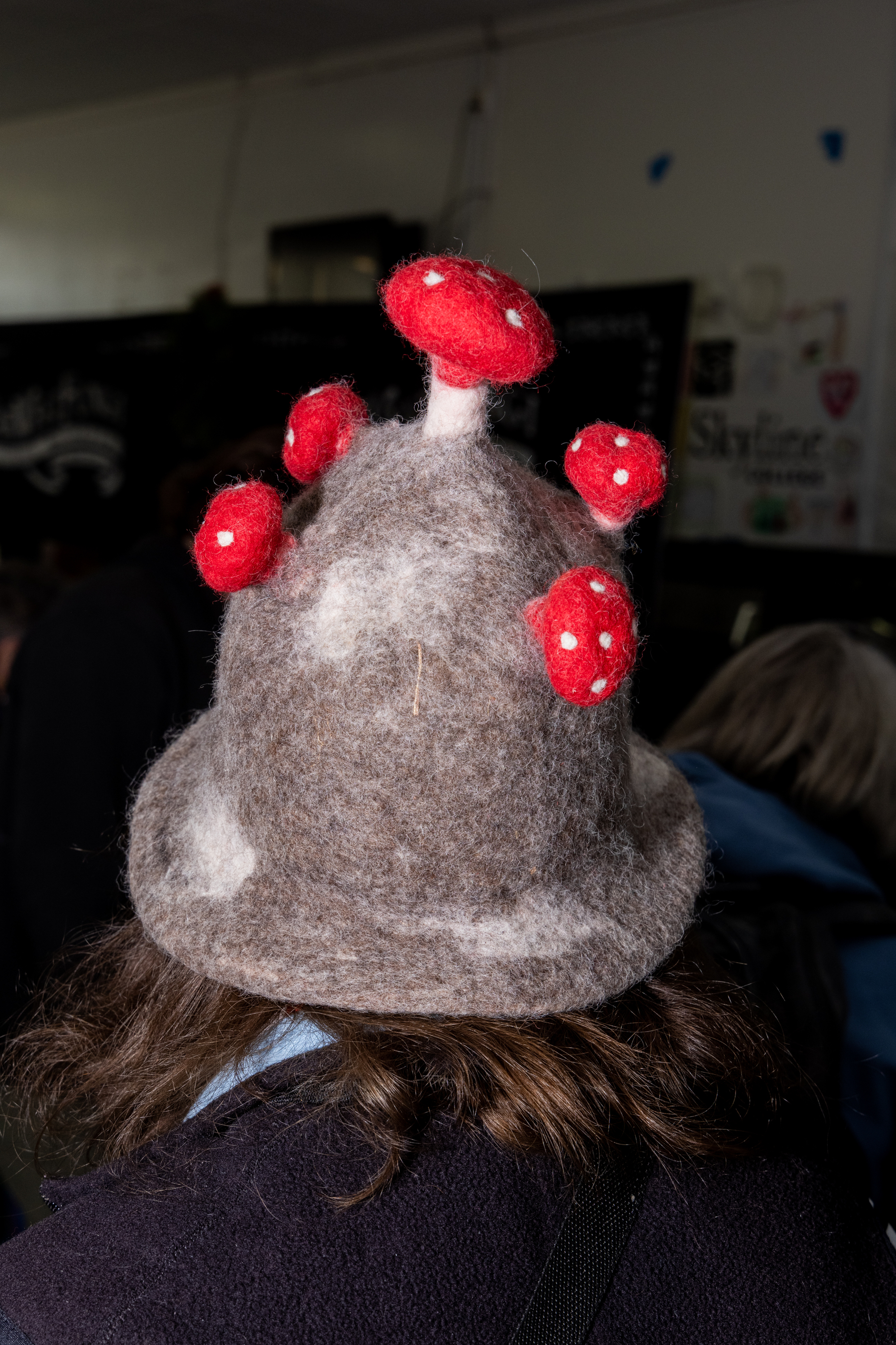 A person wears a felt hat resembling a group of brown and red mushrooms with white spots.