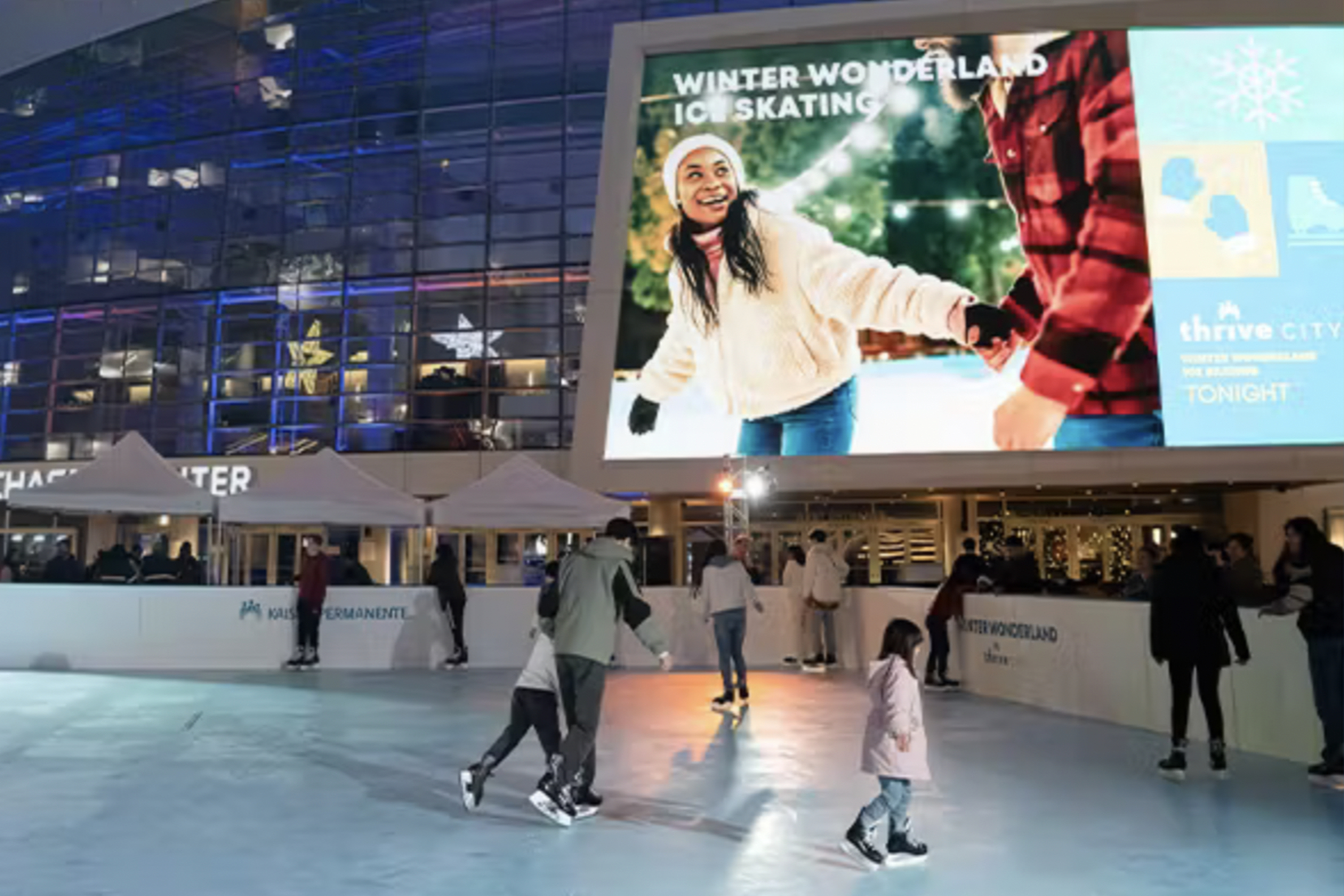 People ice skate under colorful lights with a large &quot;Winter Wonderland Ice Skating&quot; billboard above. It's a festive, lively, and vibrant scene.