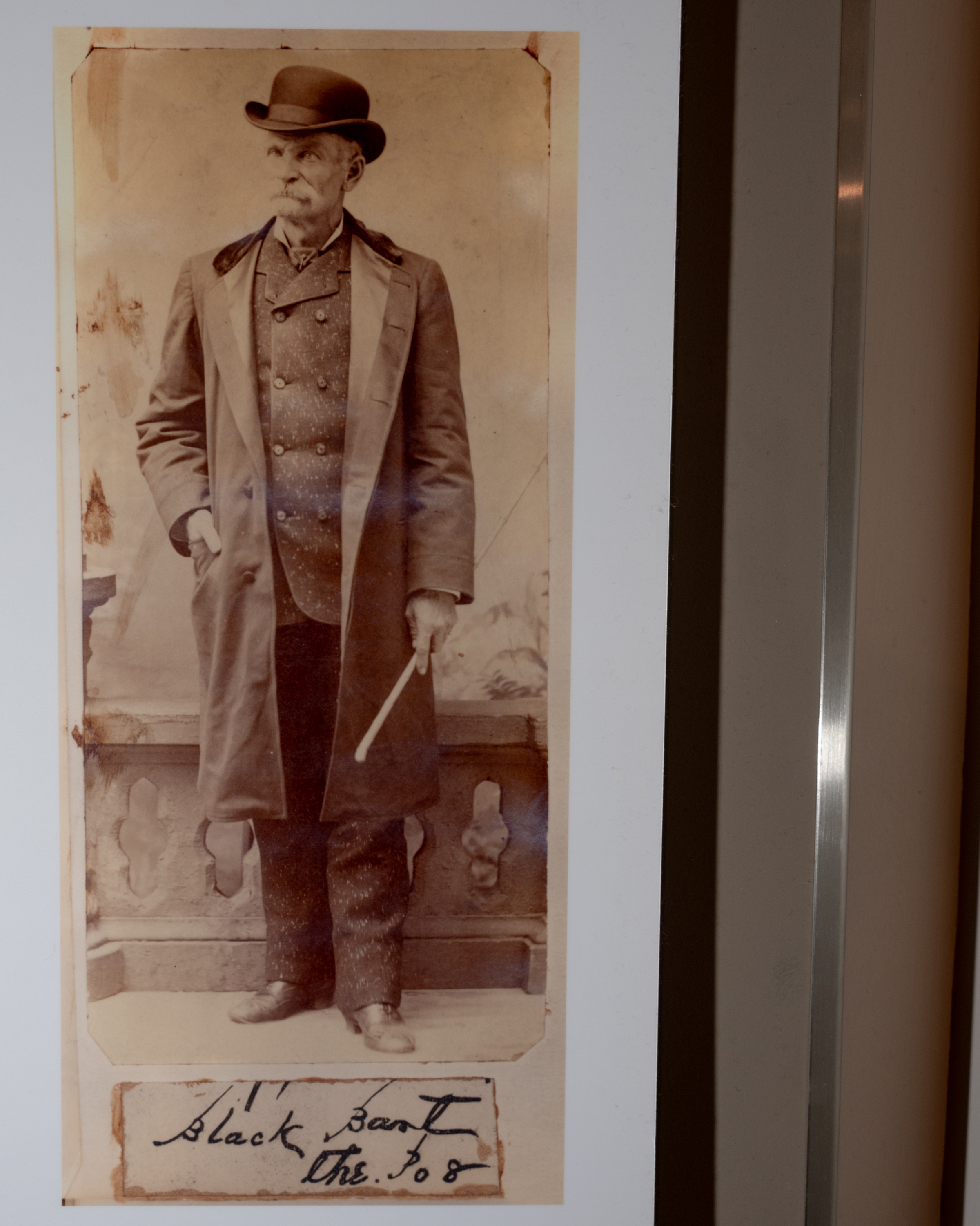 An elderly man stands, wearing a long coat and a bowler hat, holding a cane. The sepia-toned photo has a handwritten note saying &quot;Black Bart The Po8.&quot;