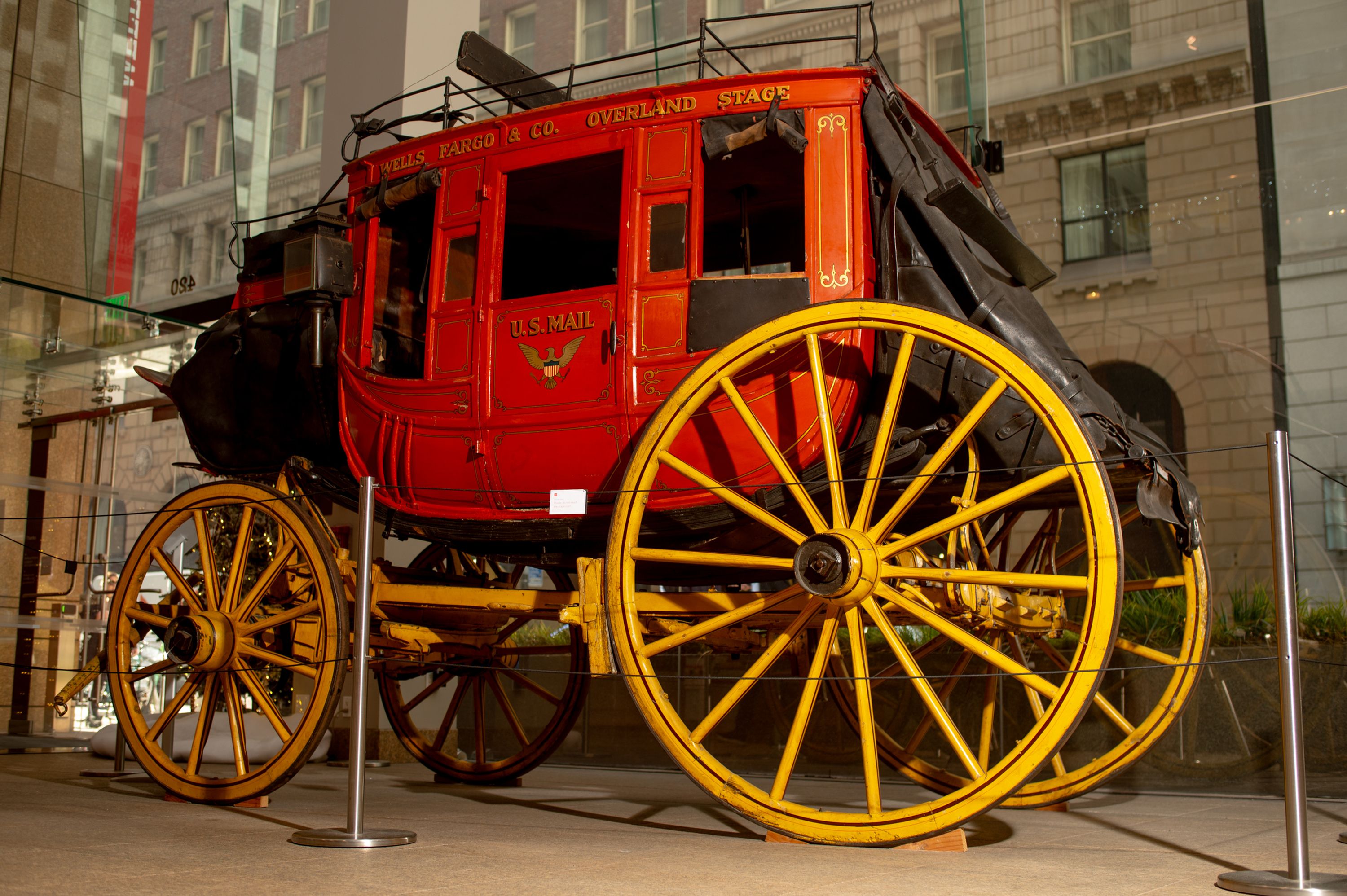 The image shows a bright red vintage stagecoach with "Wells Fargo & Co. Overland Stage" and "U.S. Mail" written on it, featuring large yellow wheels.