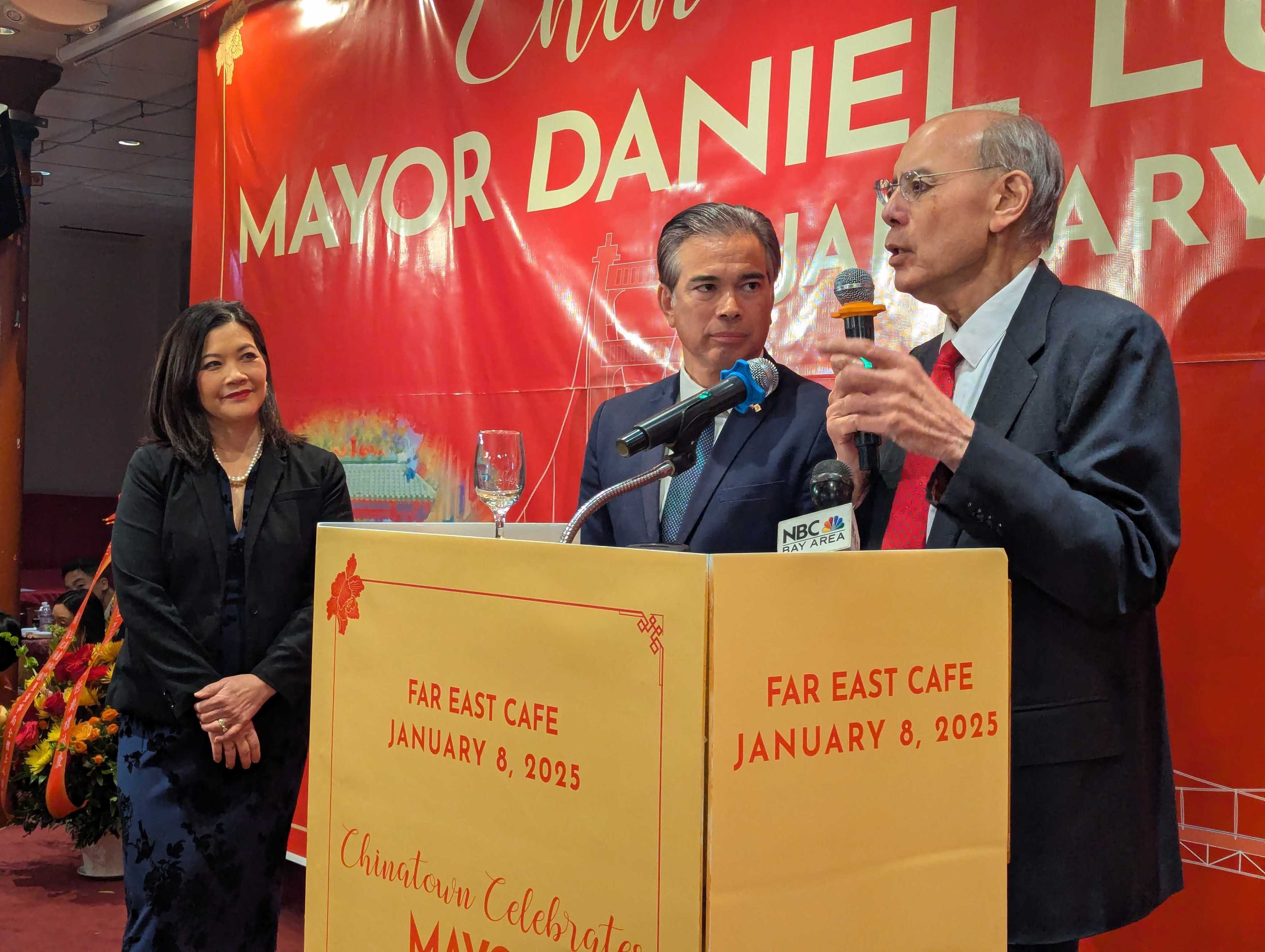 Three people are at a podium with microphones. A man is speaking, while a woman stands nearby and watches. The backdrop reads “Mayor Daniel,” dated January 8, 2025.