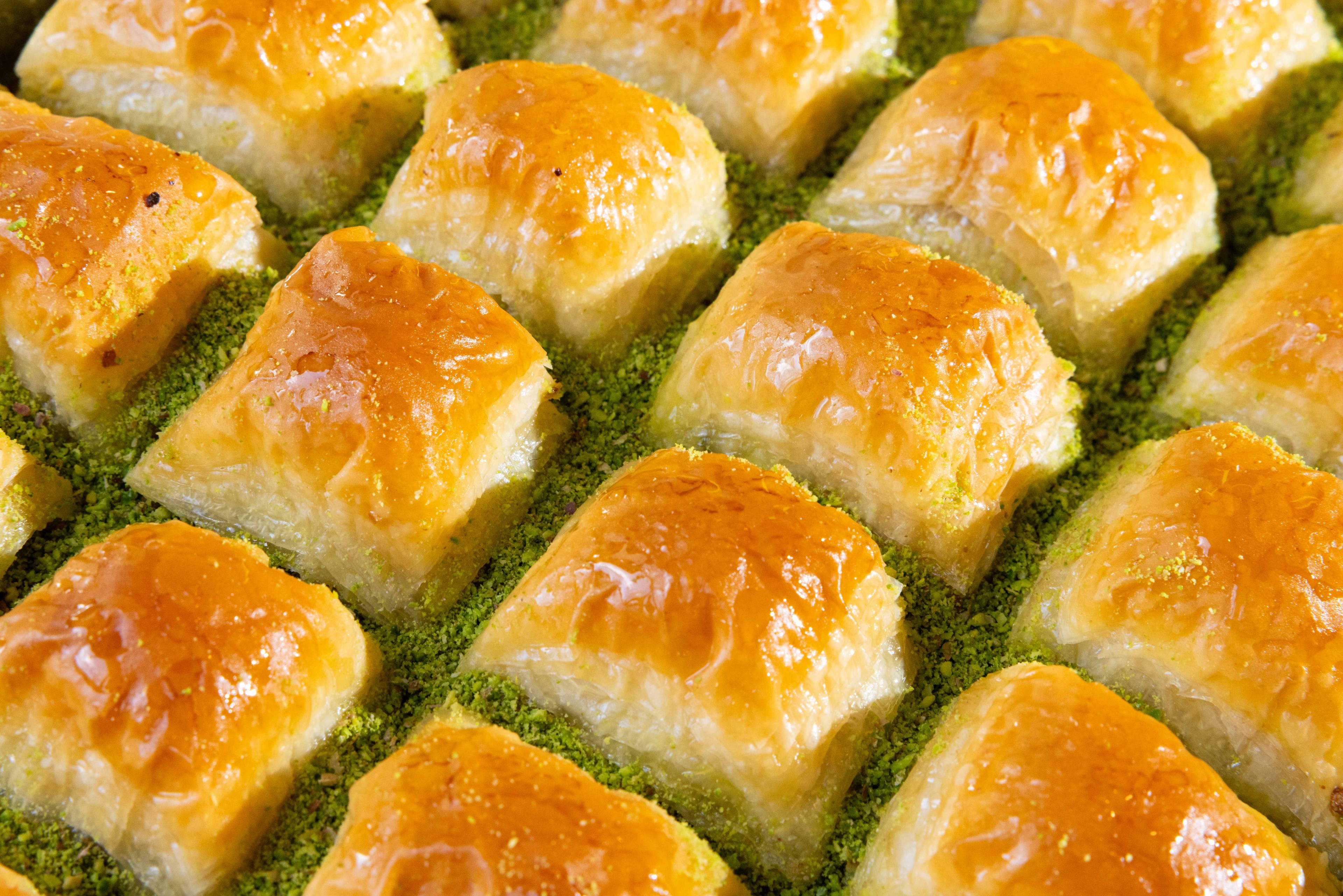 Golden, flaky baklava pieces are arranged in a grid pattern, topped with a light syrup glaze, and sprinkled with green crushed pistachios.